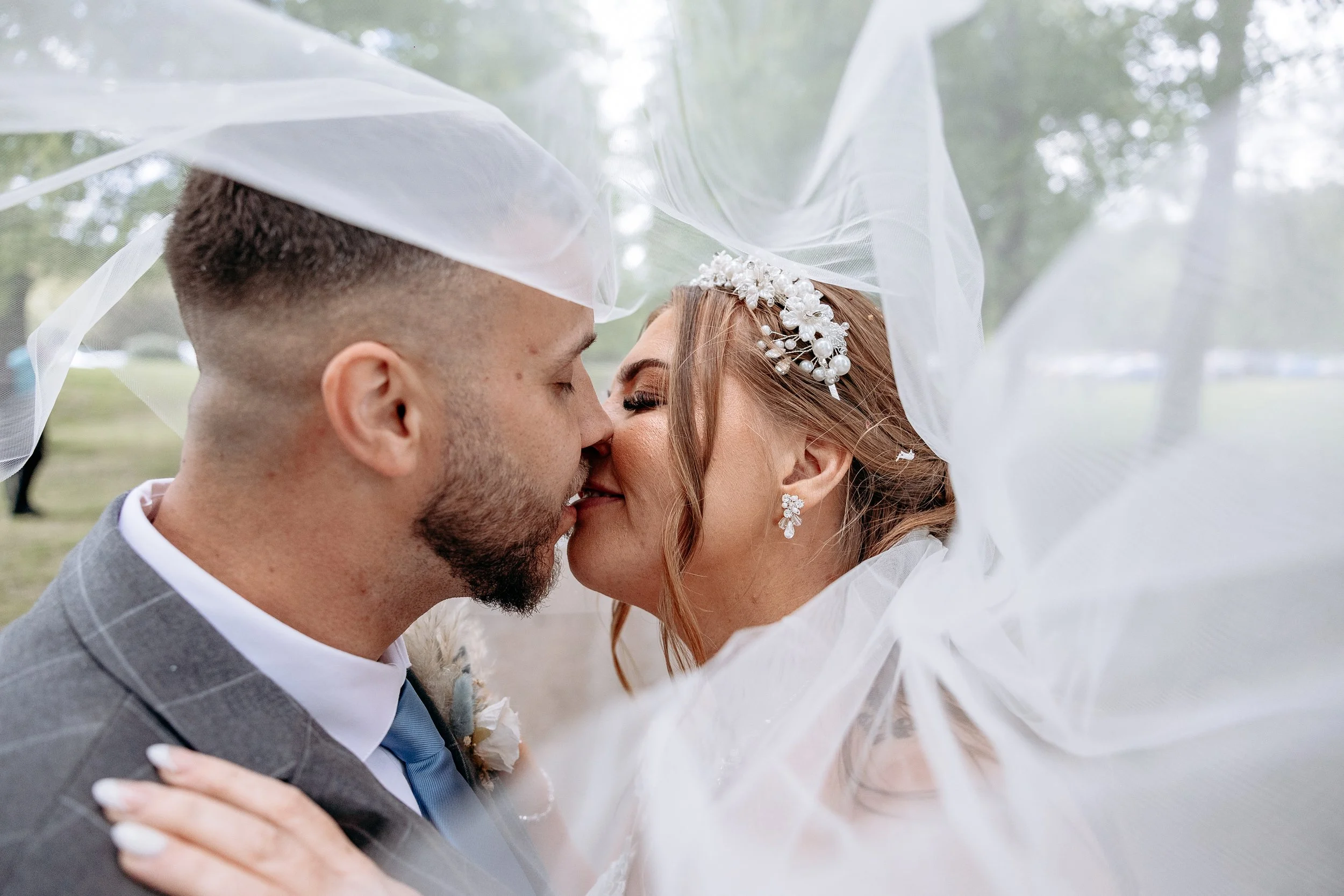 A bride and groom are close together, about to kiss, with the bride’s veil partially covering both of them.
