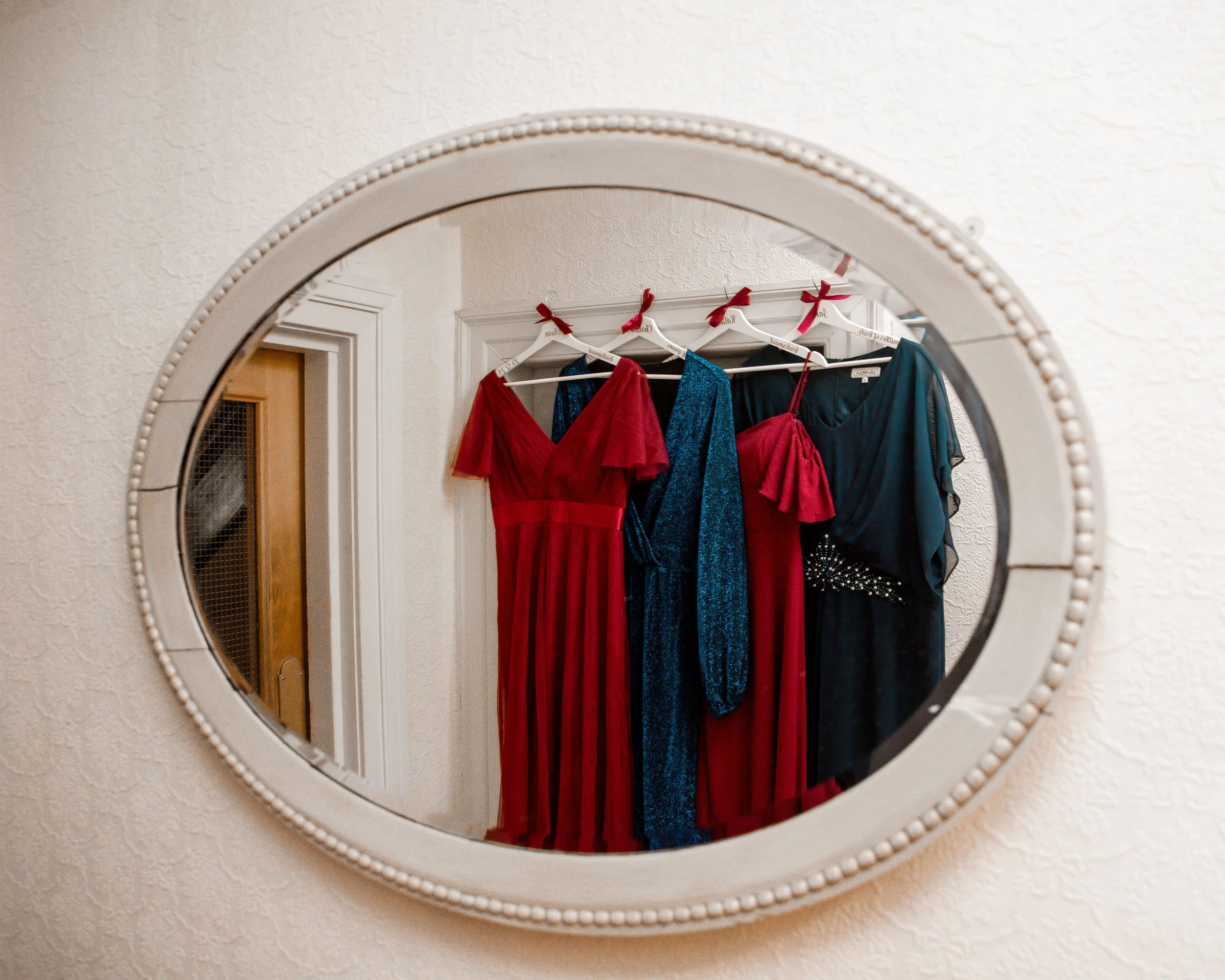 A mirror reflecting four dresses hanging on a wall, including red, blue, and black dresses with various designs and embellishments.