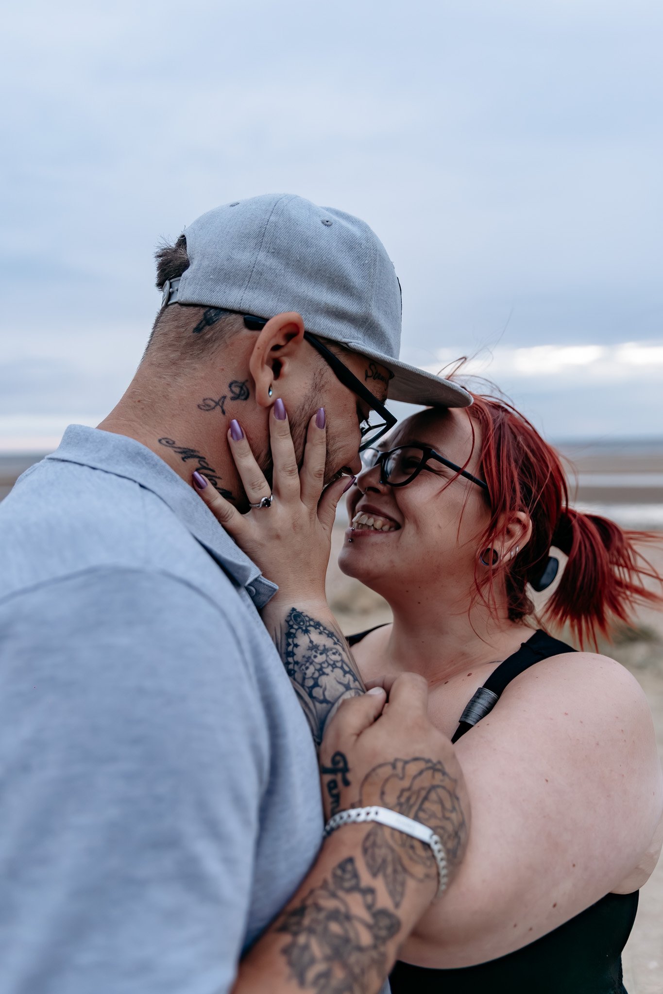 A couple shares a close, intimate moment on a beach, with their foreheads and noses touching, smiling at each other.