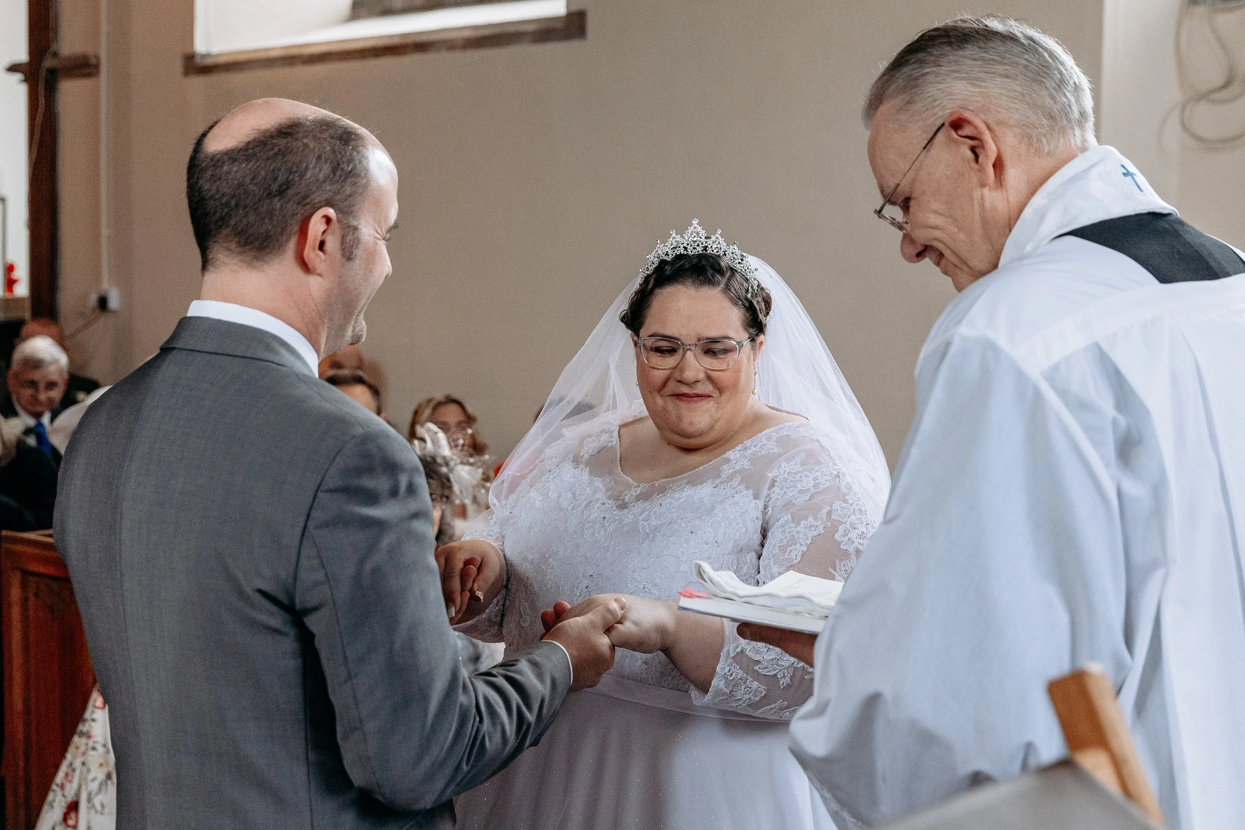 Bride and groom exchanging wedding vows, with a priest officiating the ceremony inside a church.