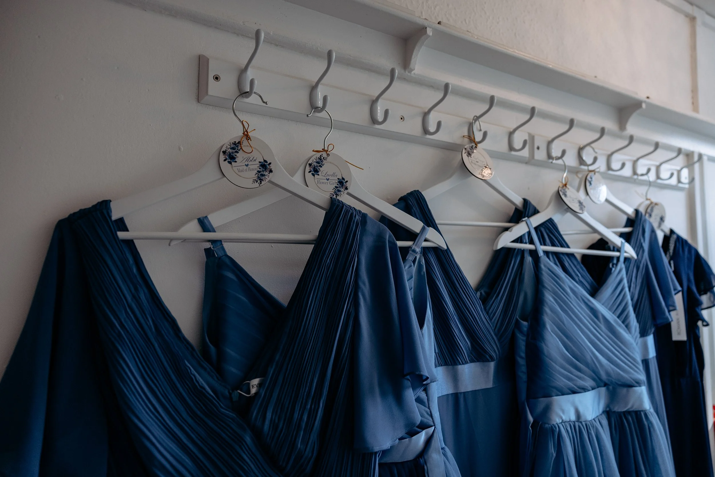 Multiple blue bridesmaid dresses hanging on white hangers on a hook rack