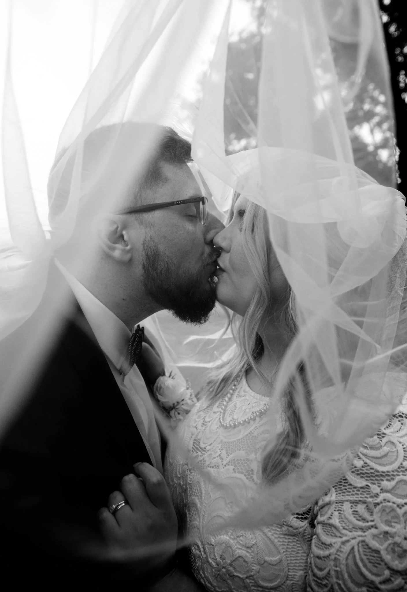 Bride and groom kissing under veil in black and white.
