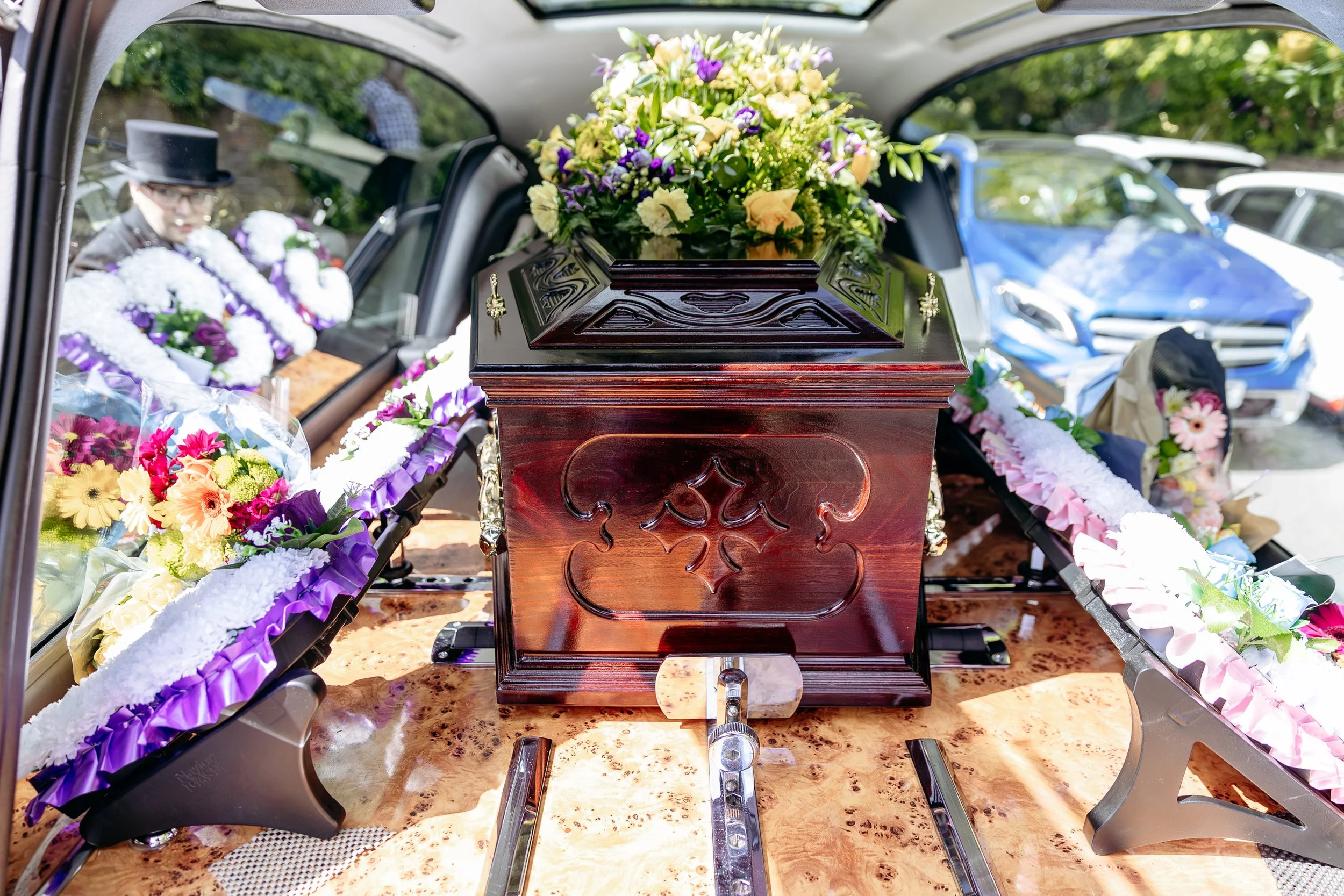 A casket decorated with flowers inside a hearse, prepared for a funeral procession.