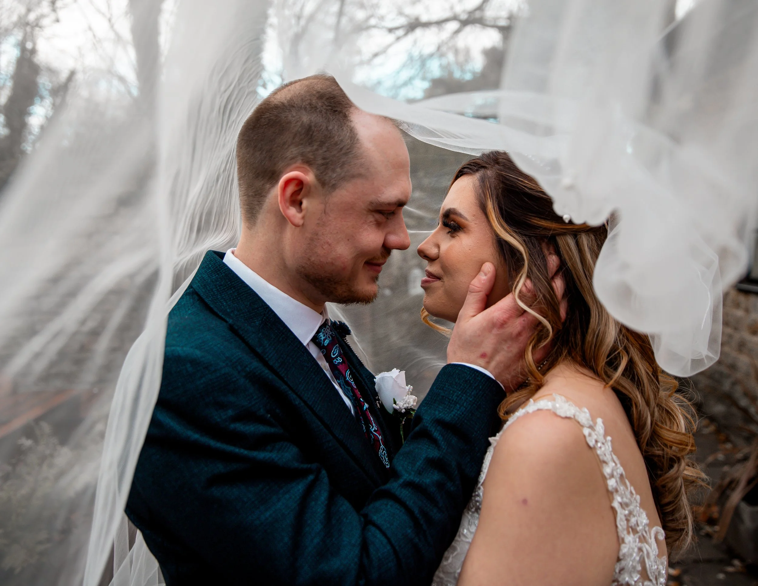 A bride and groom gazing into each other's eyes under the bride's veil, with the groom gently holding the bride's face.
