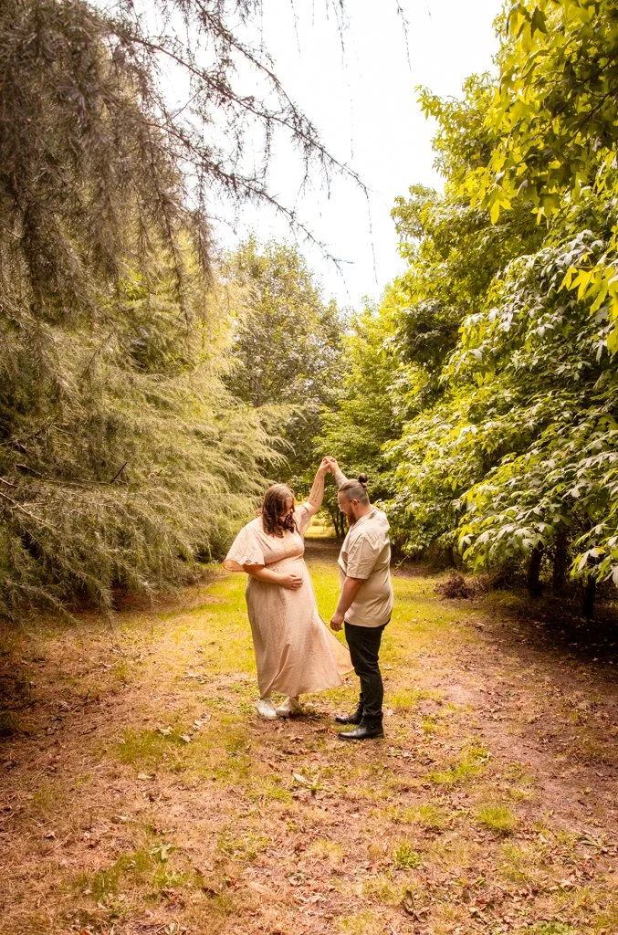 A couple dances together on a dirt pathway surrounded by green trees and foliage in a peaceful outdoor setting.