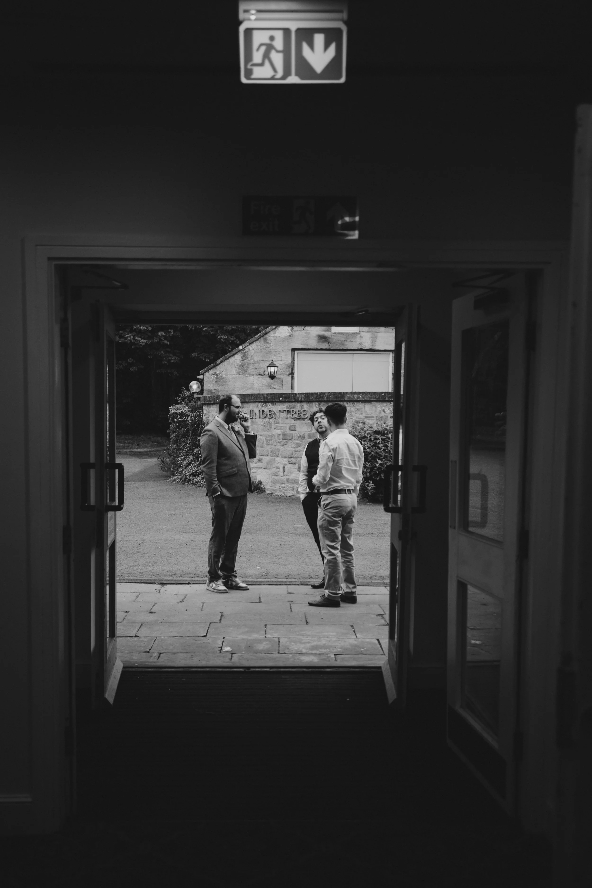 Three men dressed in business casual attire standing outside and engaged in conversation, visible through a doorway.