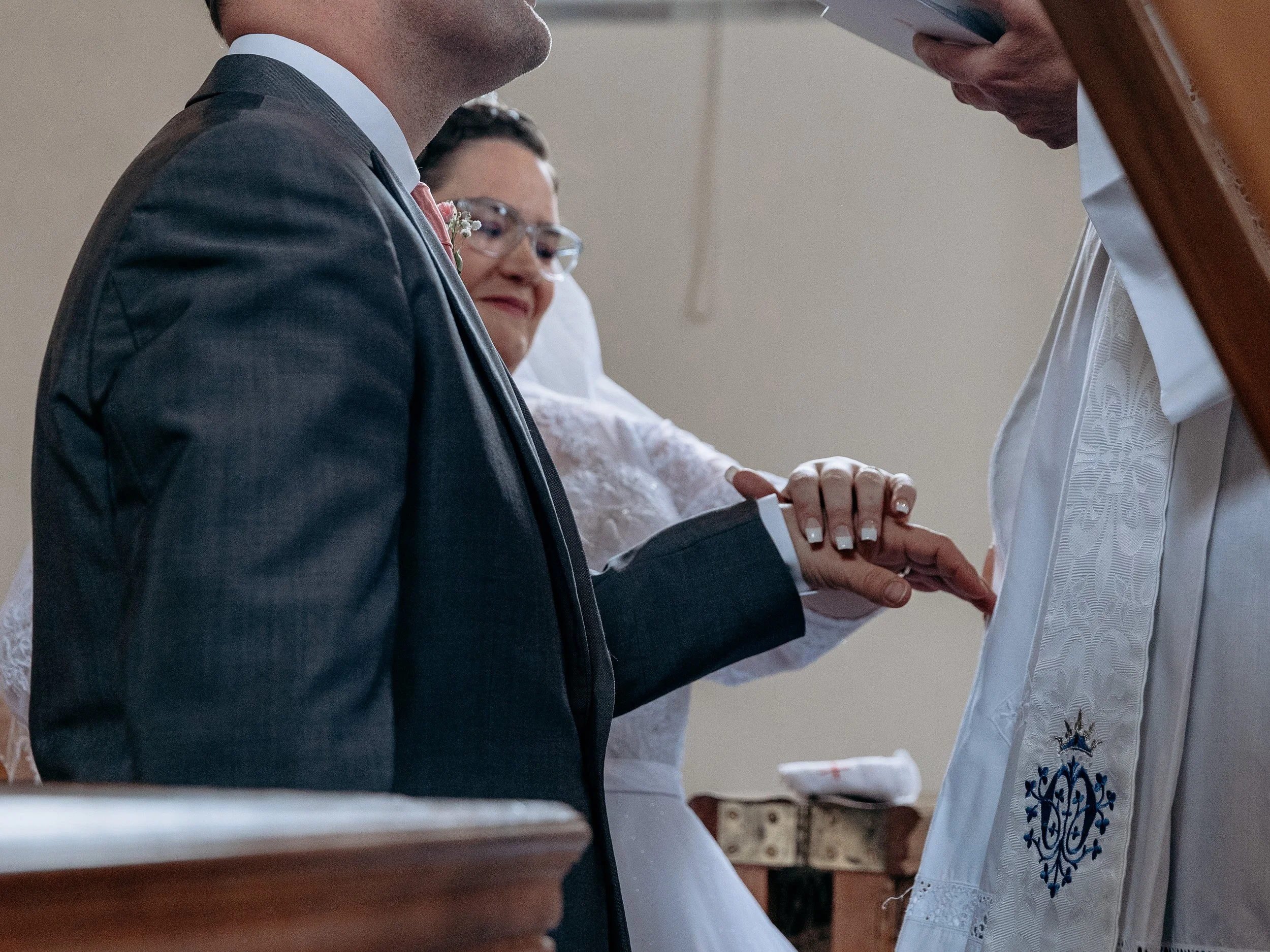 A couple getting married holding hands during the wedding ceremony, with a priest present.
