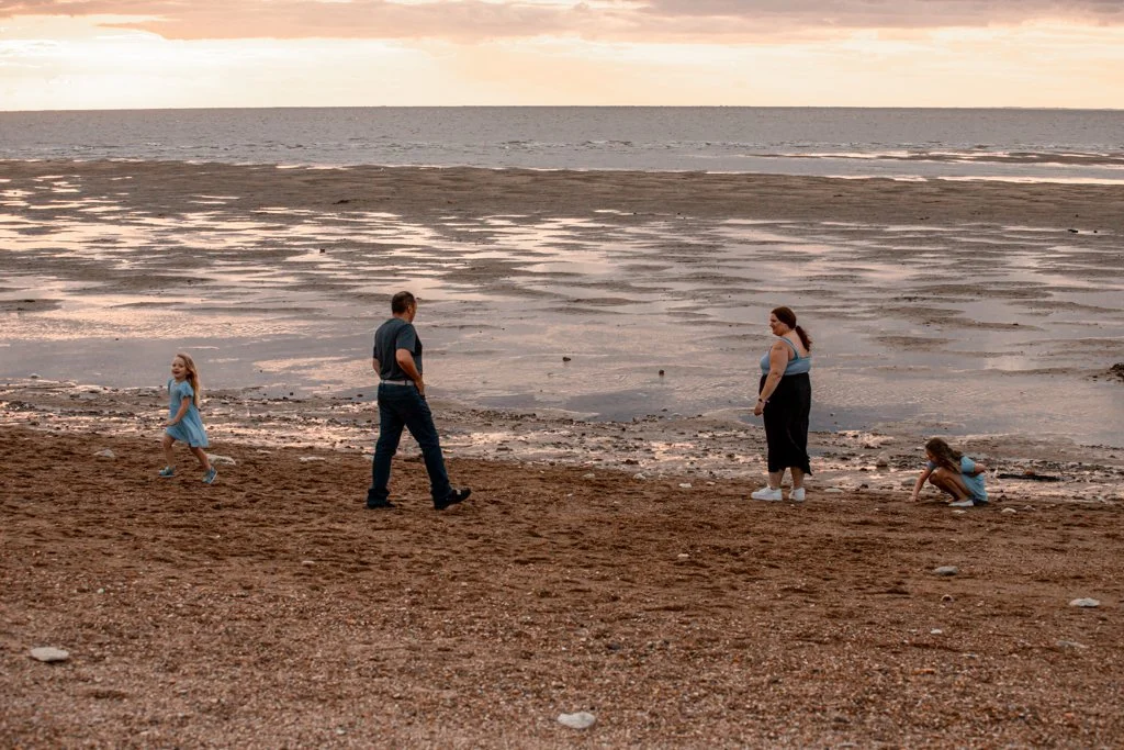Family walking on a sandy beach at sunset with tide out; two children playing.