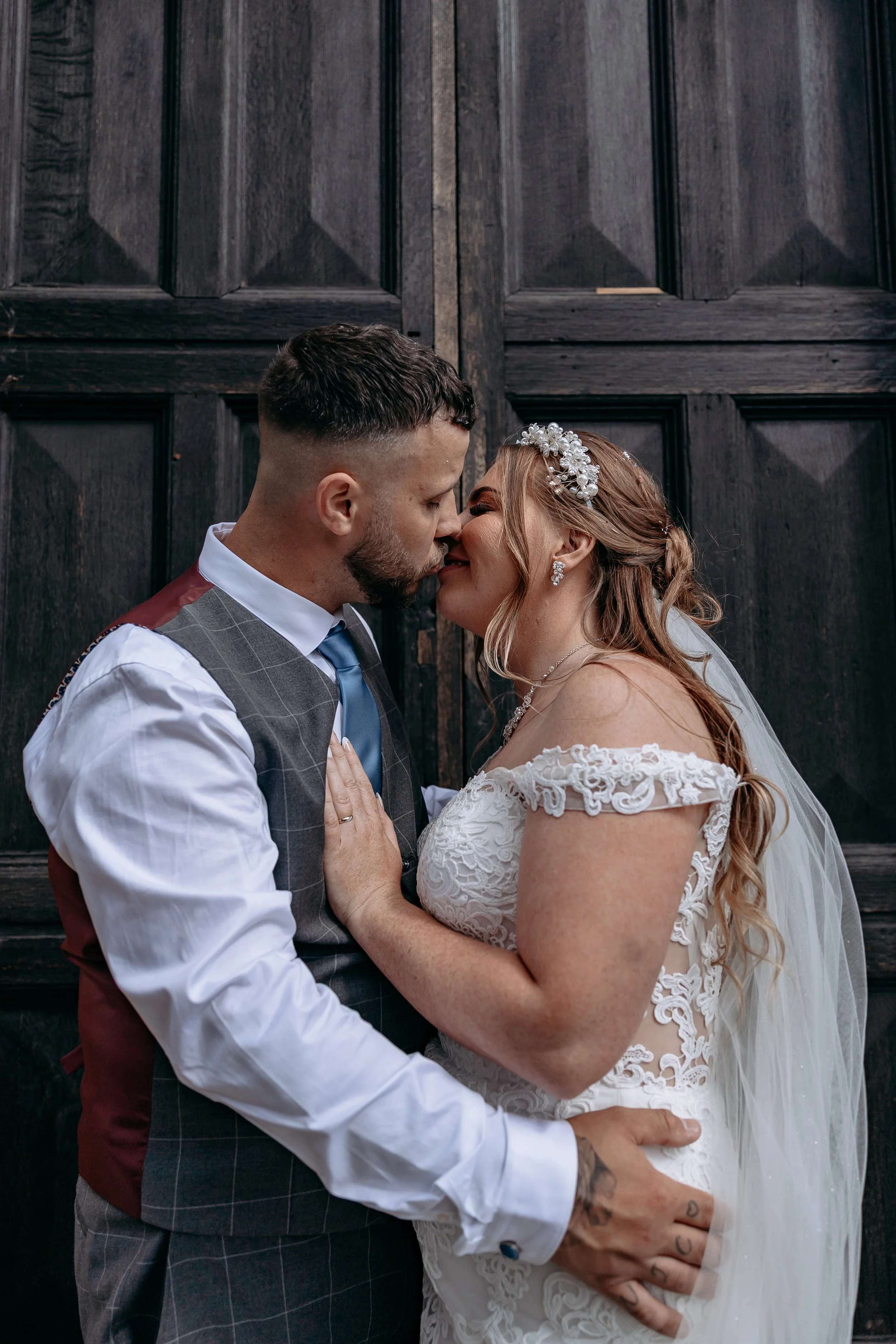 A bride and groom kissing in front of dark wooden doors on their wedding day.