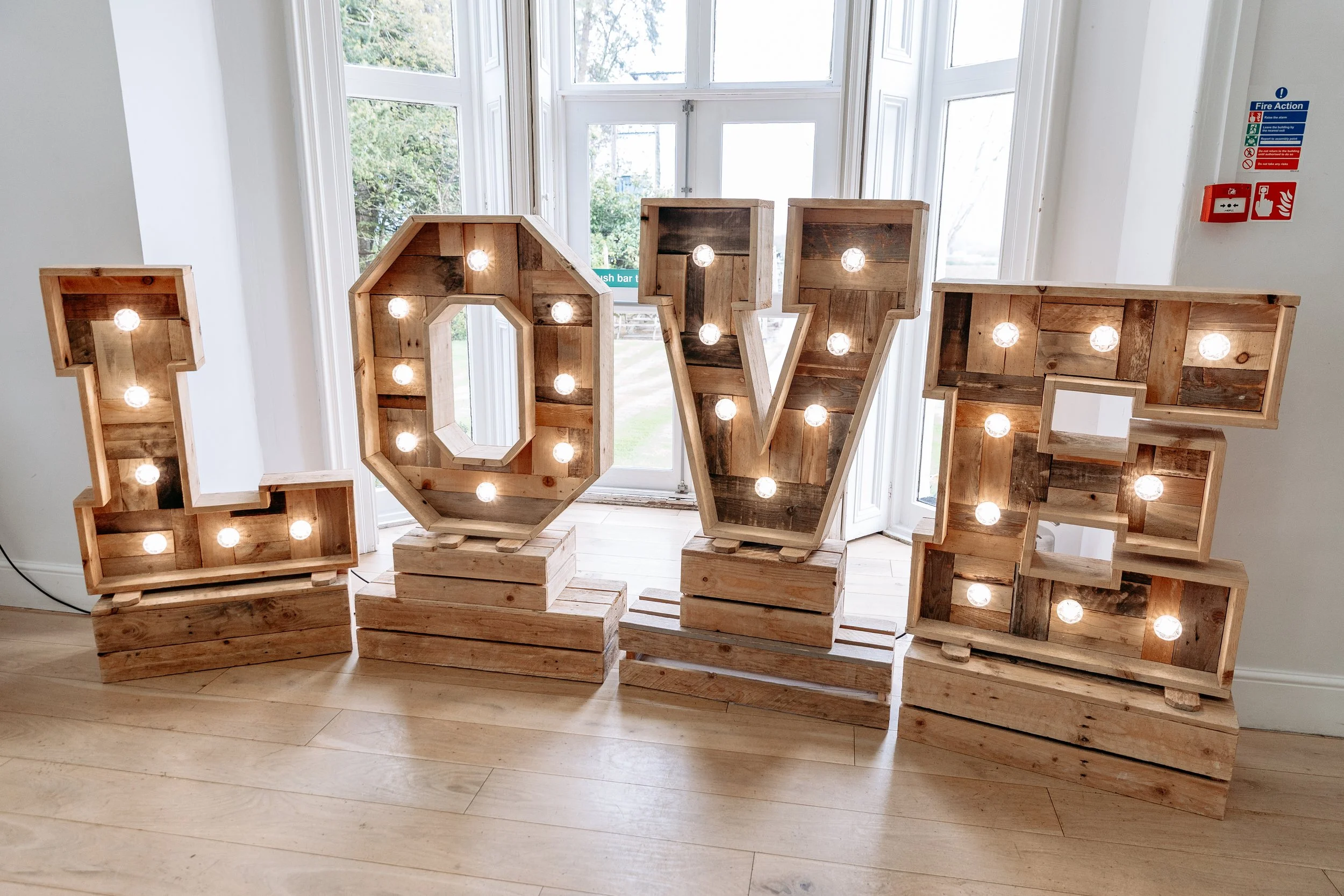 Large decorative letters spelling 'LOVE' made of wood with light bulbs inside, displayed indoors near windows.