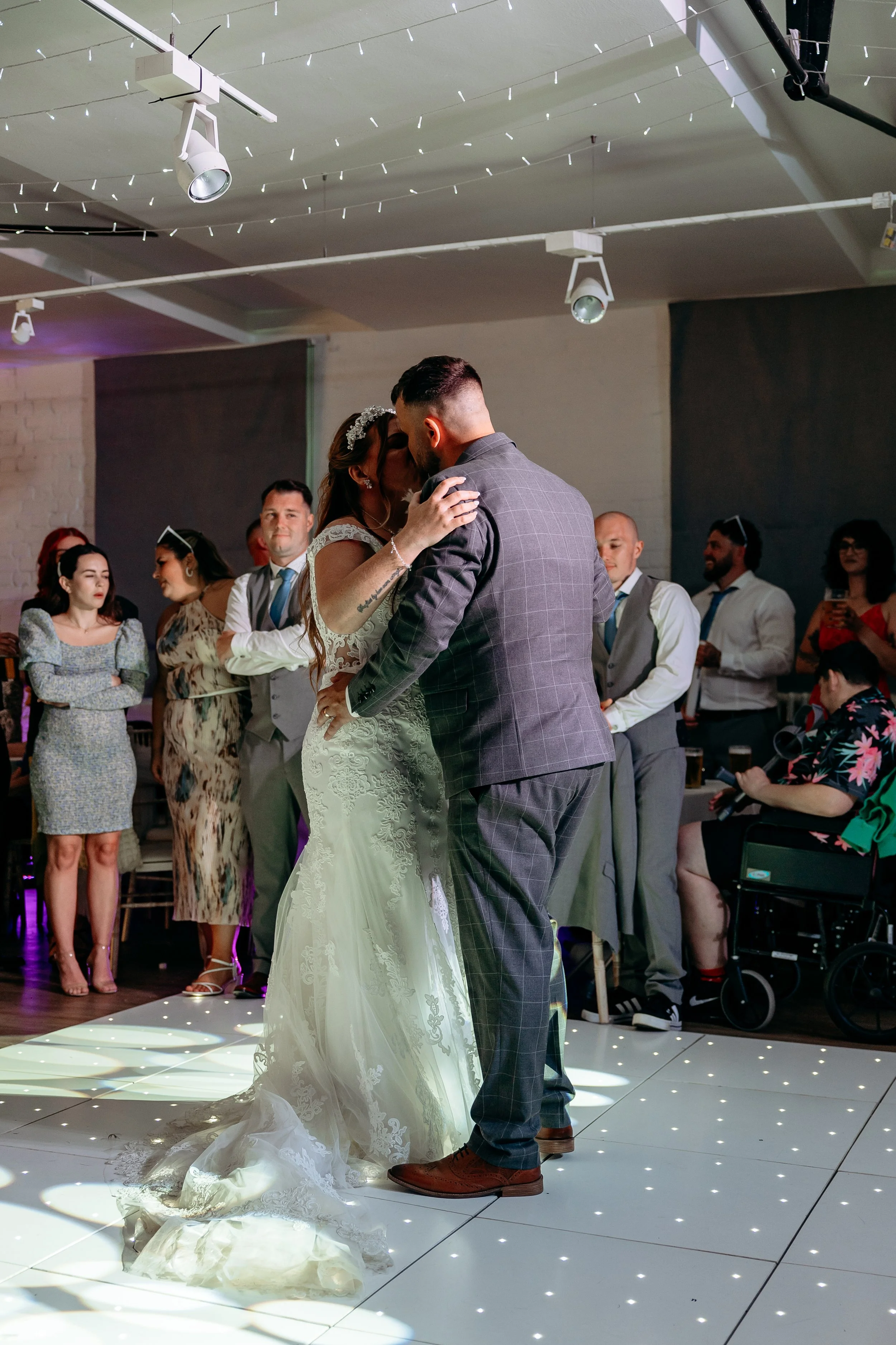 A bride and groom share their first dance at a wedding reception, surrounded by guests in an indoor event space.
