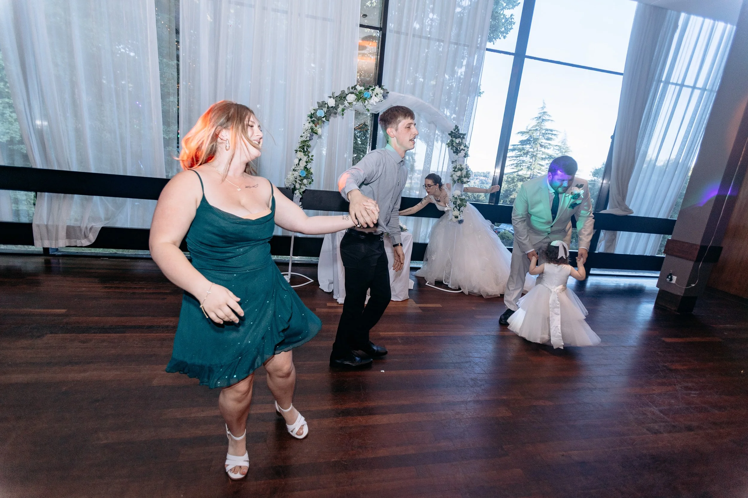 People dancing at a wedding reception with a bride by a decorated arch.