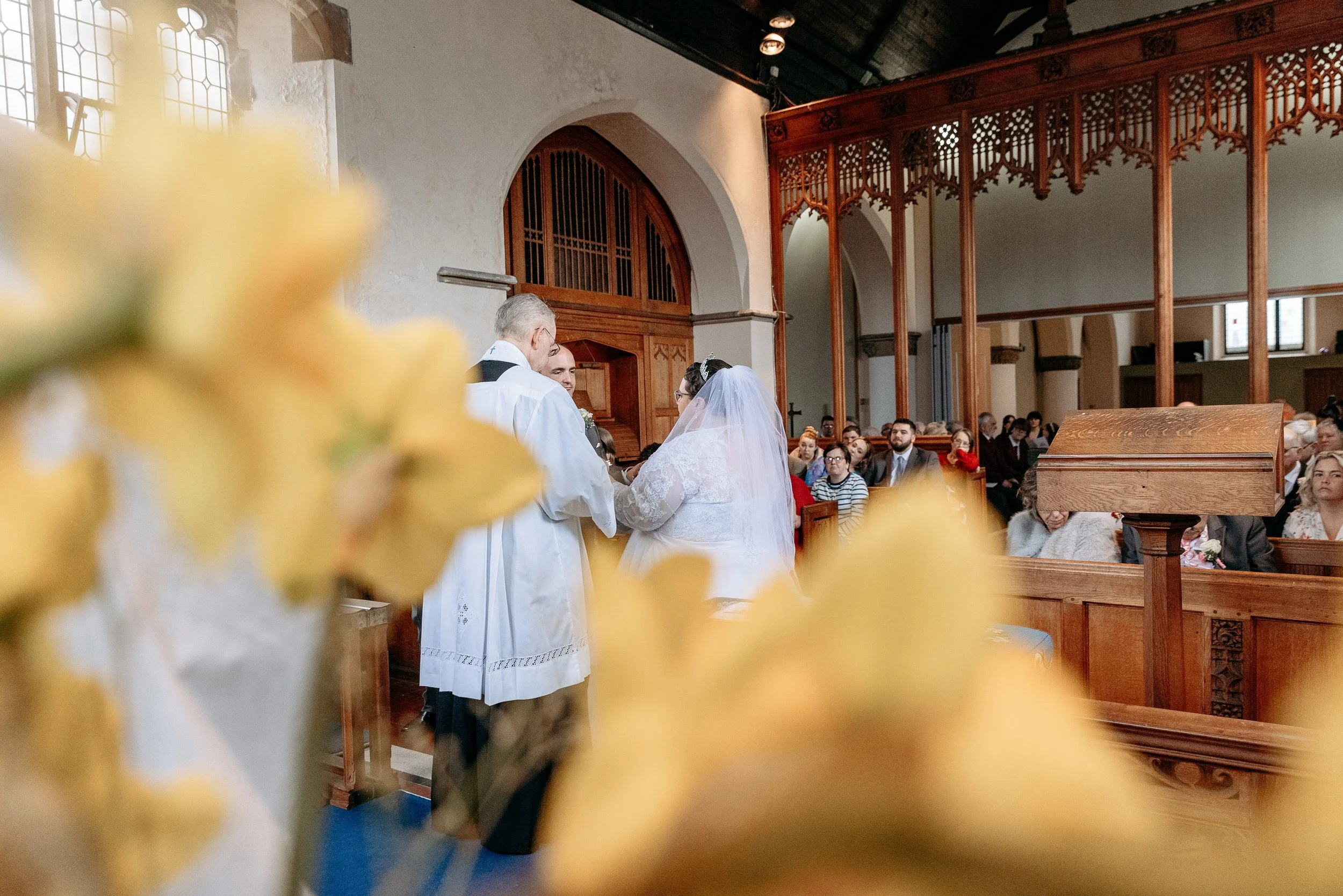 A wedding ceremony taking place inside a church, with the bride and groom standing at the altar, surrounded by guests seated in wooden pews.
