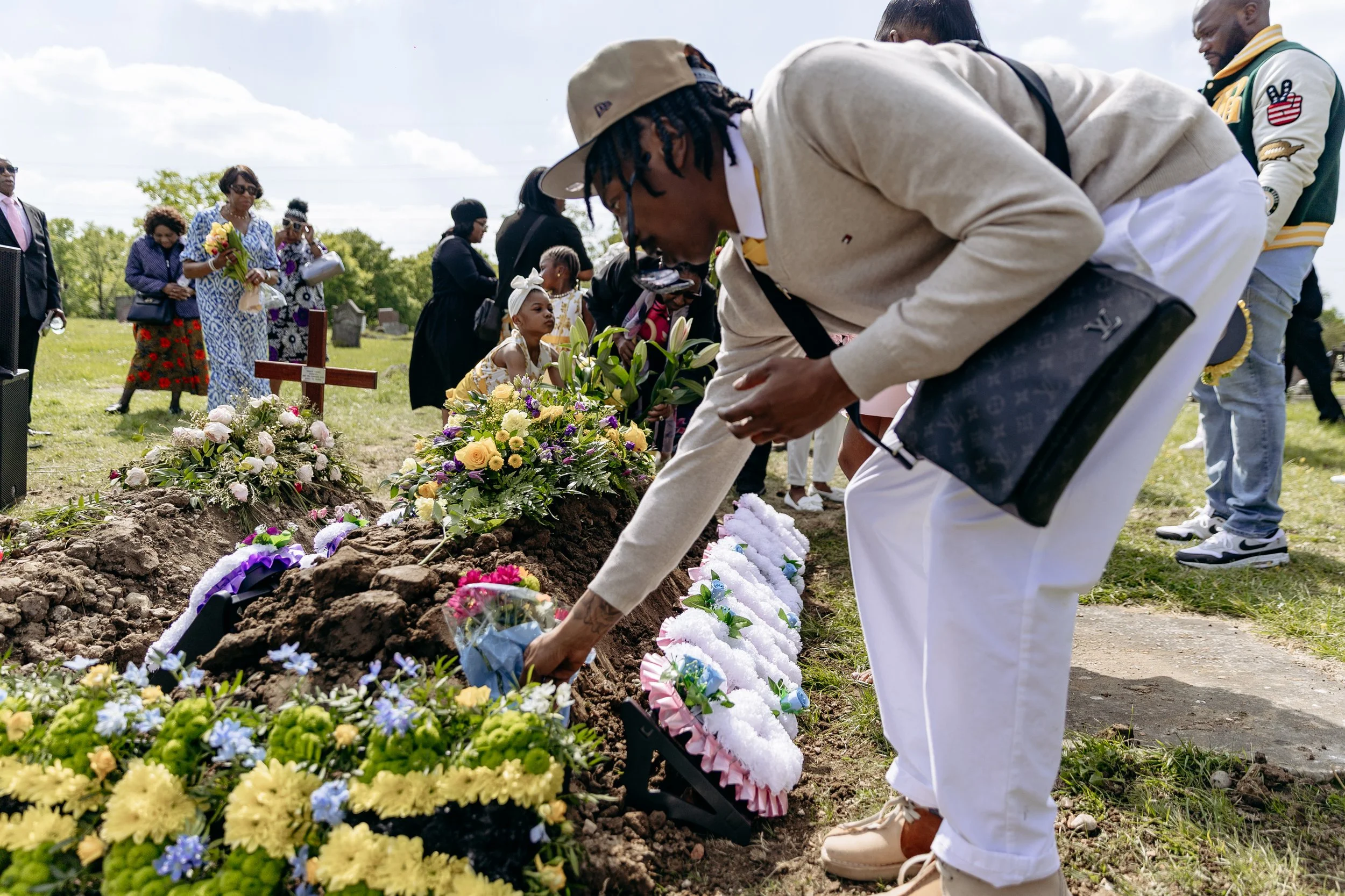 People placed flowers on a grave during a funeral in a grassy cemetery on a cloudy day.