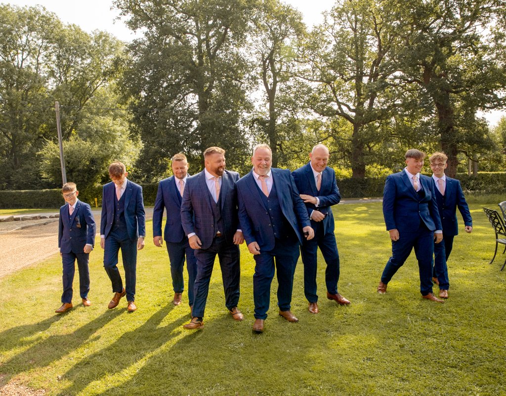 Group of eight men dressed in blue suits walking outdoors on a sunny day, with trees in the background.