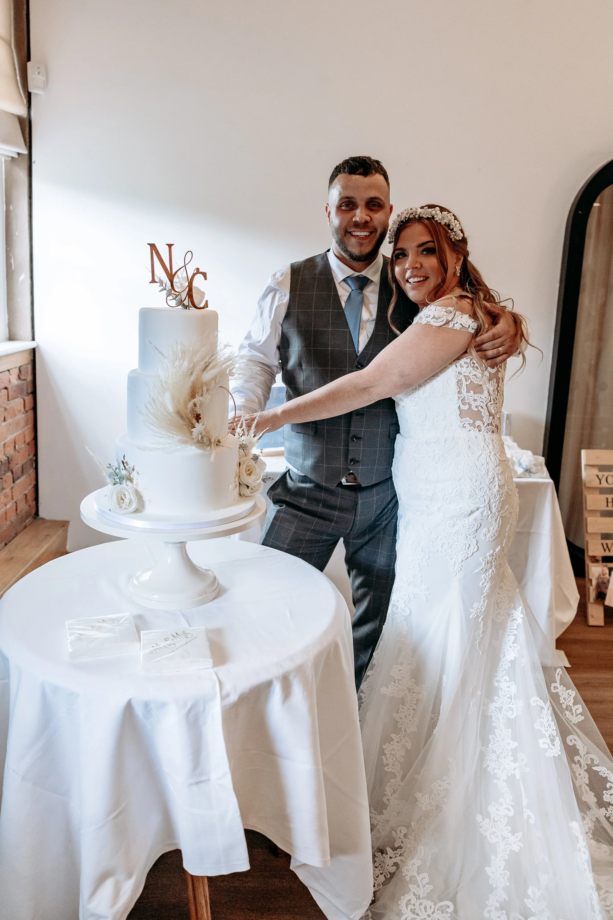 A newlywed couple in wedding attire cutting a wedding cake together, smiling, with a 