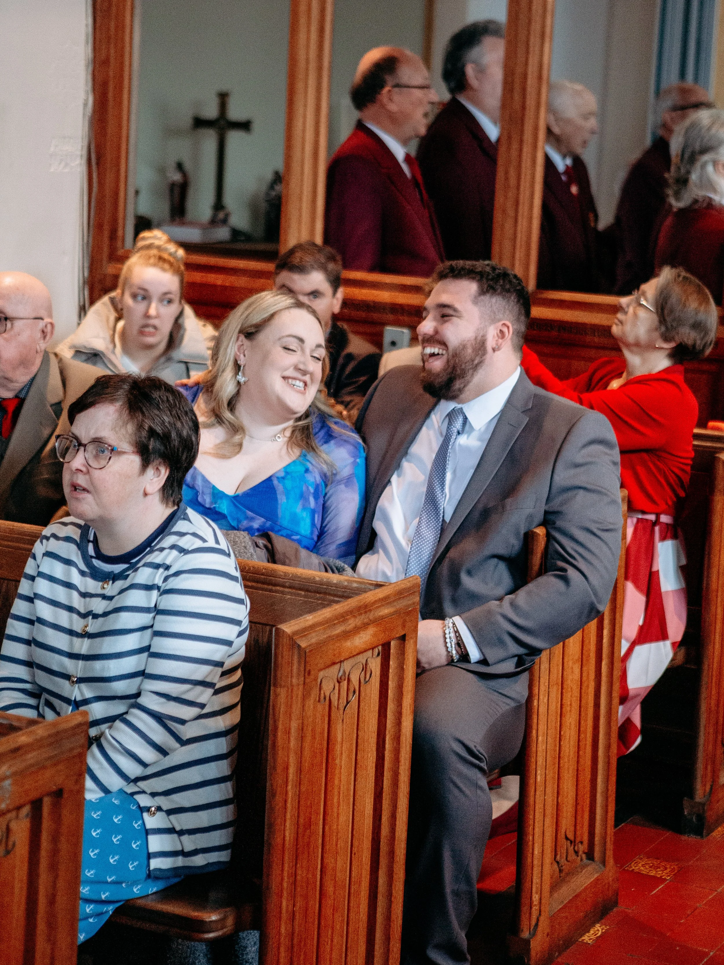 People smiling and laughing sitting in wooden pews inside a church.