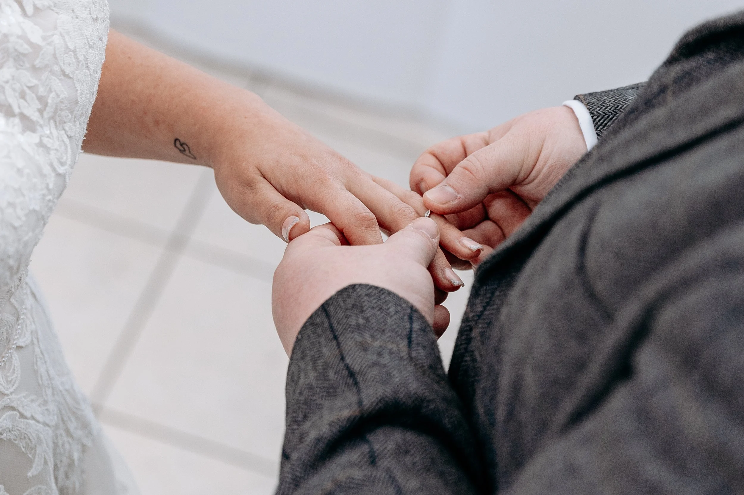 A person is placing a wedding ring on another person's finger during a wedding ceremony.