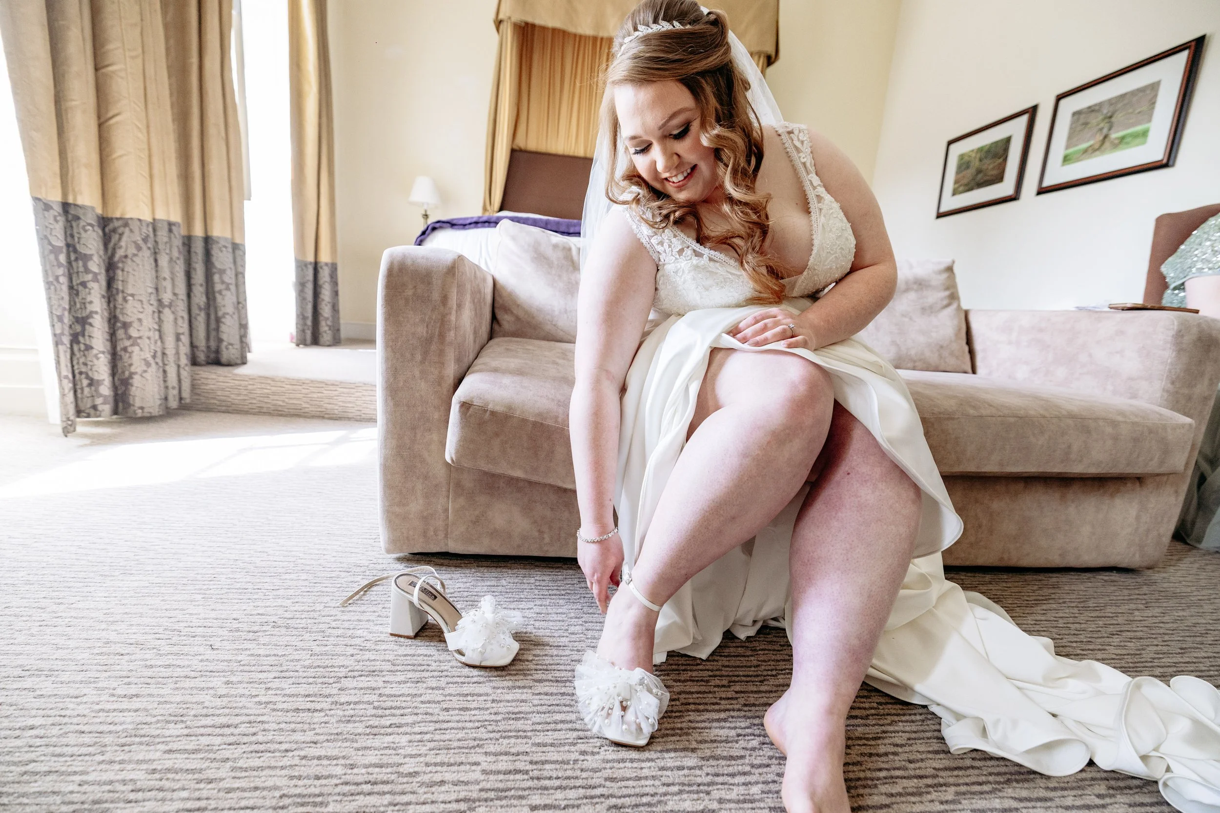 Bride in a white wedding dress putting on her shoes in a hotel room.