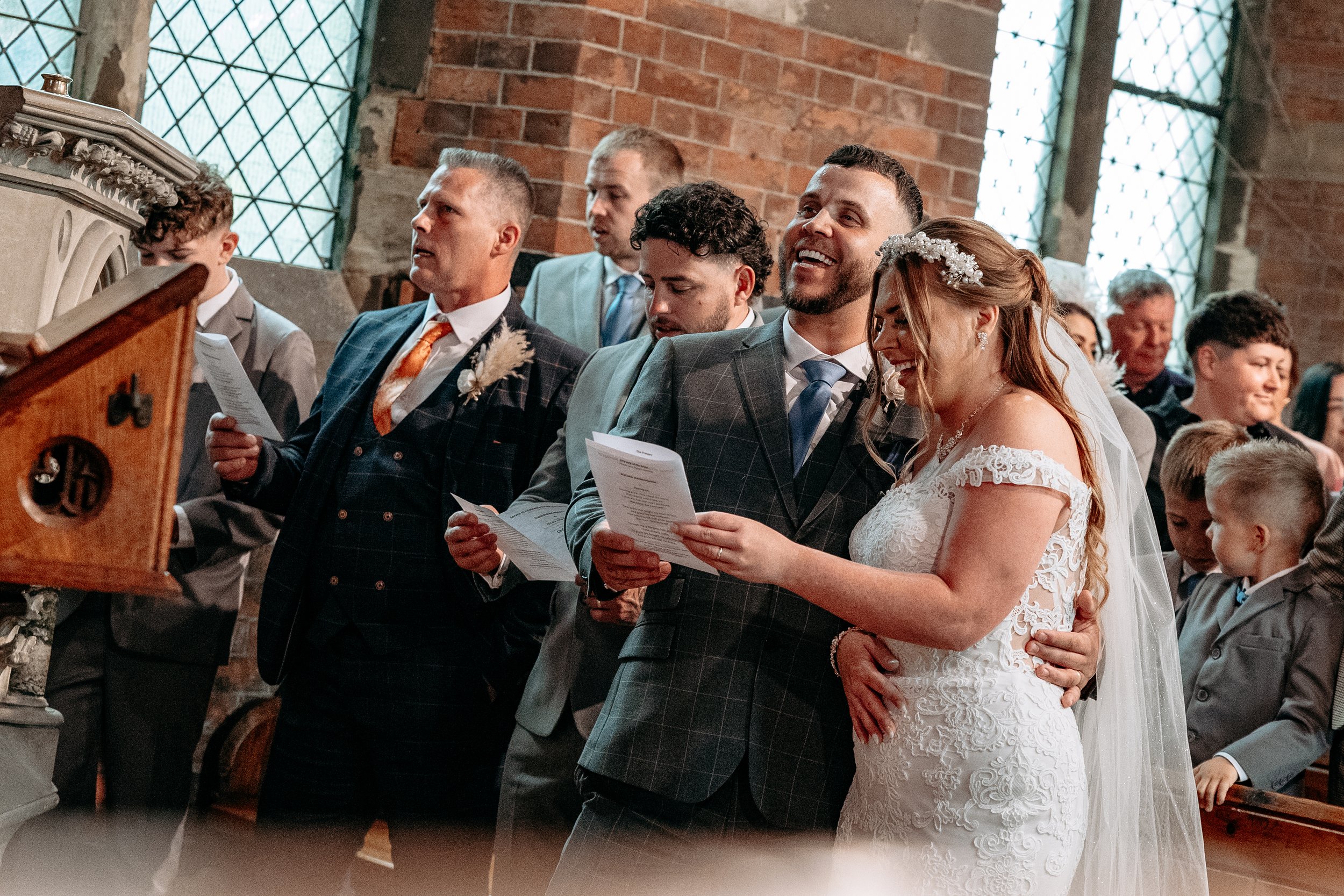 A bride and groom reading vows during their wedding ceremony inside a church, surrounded by family and friends.