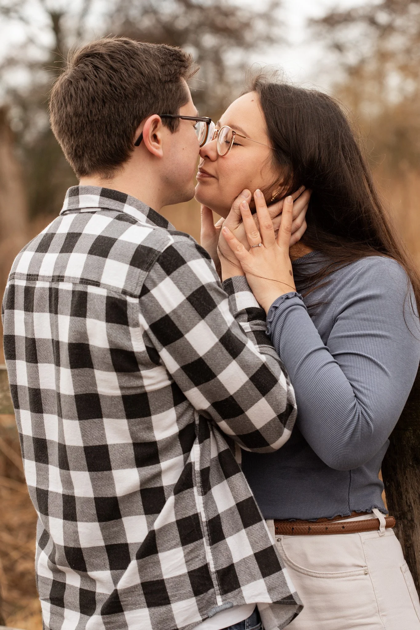 A young man and woman are intimately close, about to kiss outdoors in a natural setting, with trees in the background.