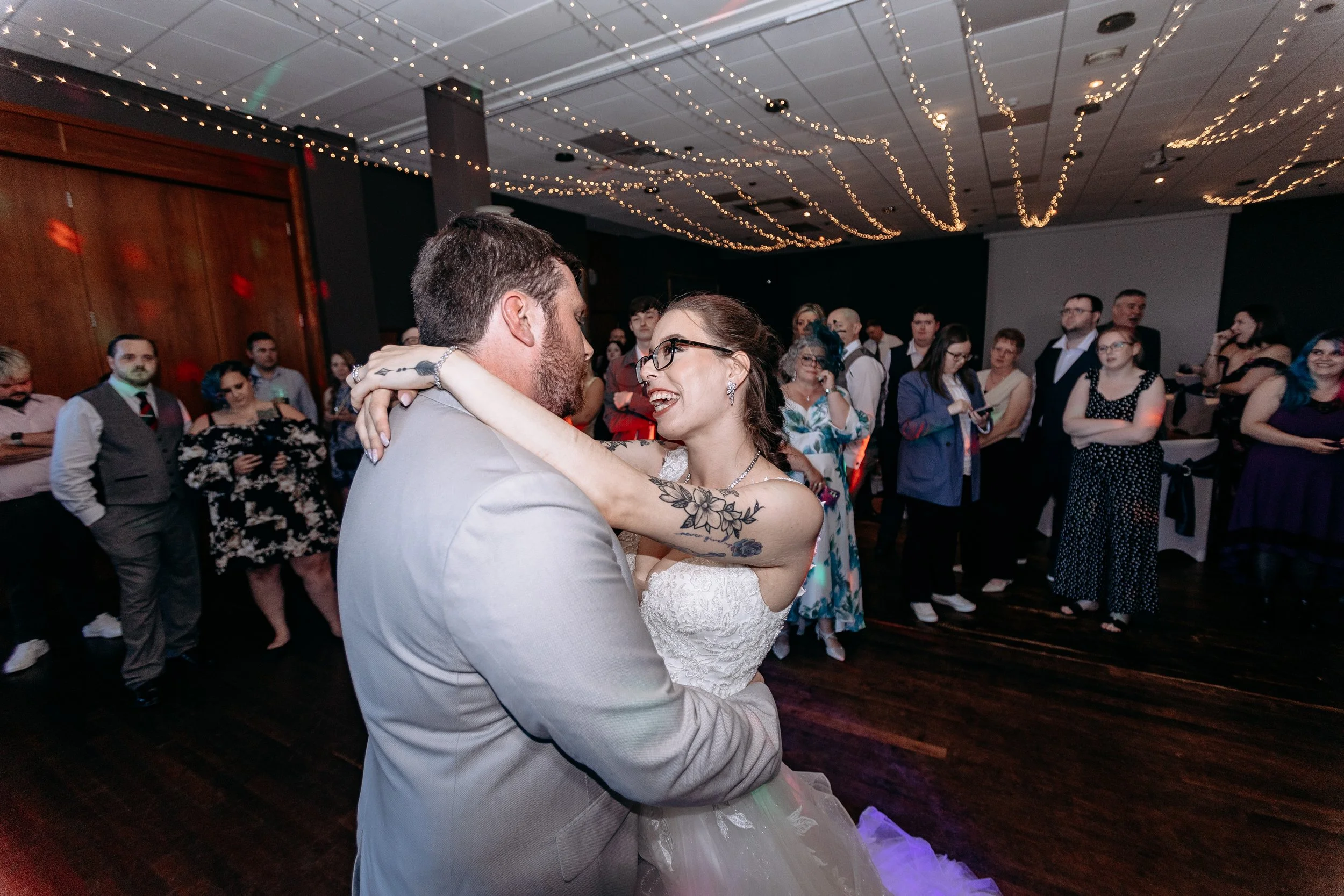 Bride and groom dancing at a wedding reception, surrounded by guests in a decorated venue.