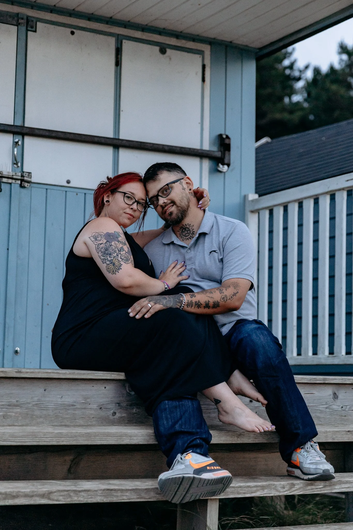 A couple sitting on wooden steps outside, hugging and gazing at the camera.