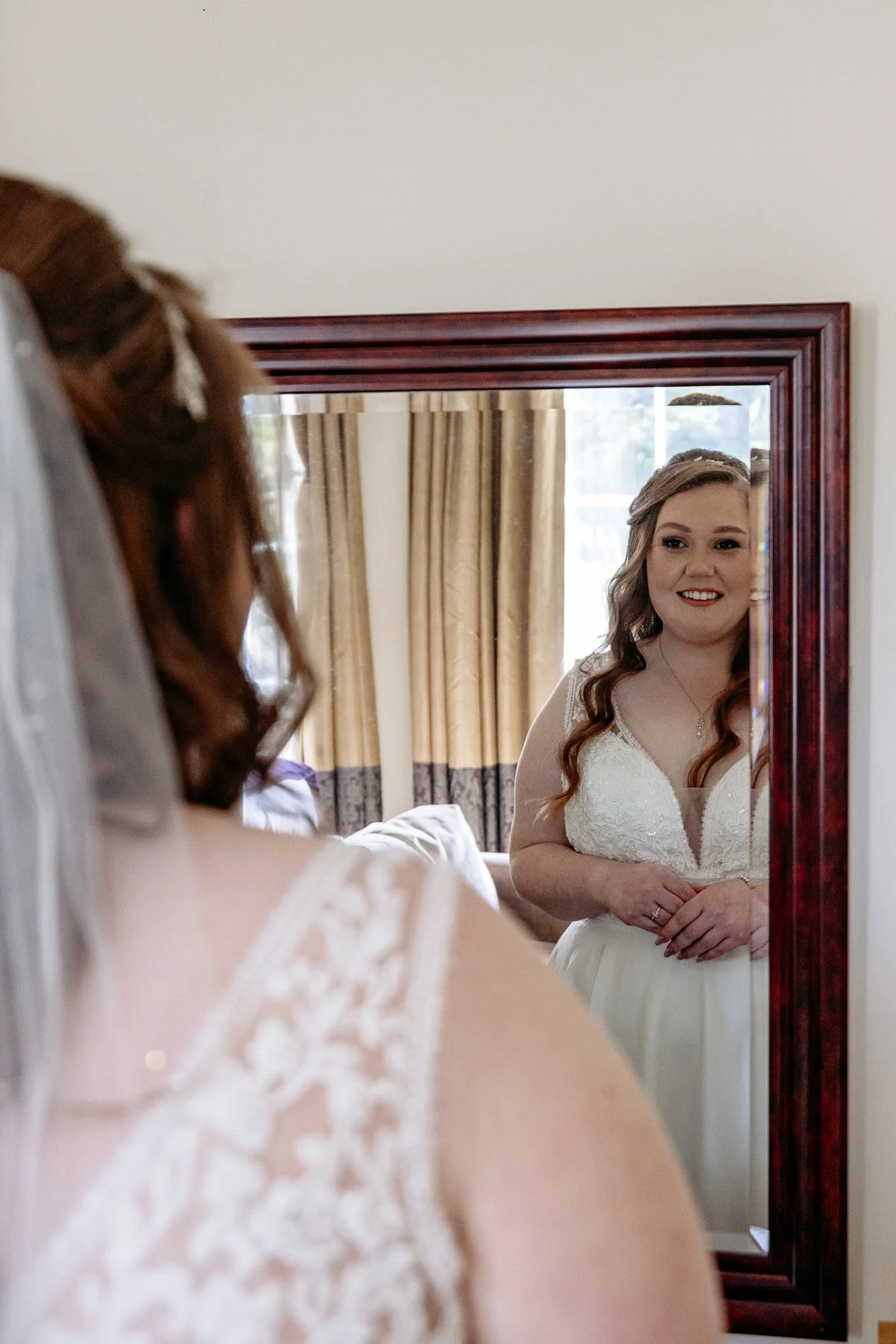 A bride looking at herself in a mirror and smiling.