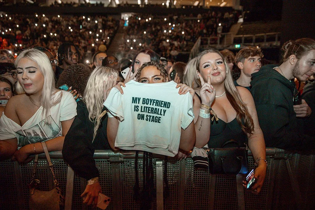 Concert audience with person holding "My boyfriend is literally on stage" shirt.