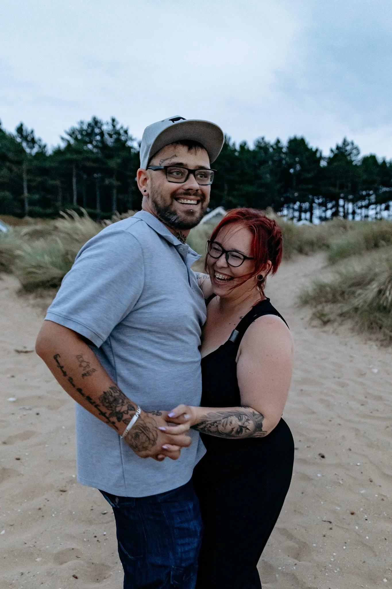 A happy couple sharing a joyful moment on the beach during the evening, holding hands and smiling.