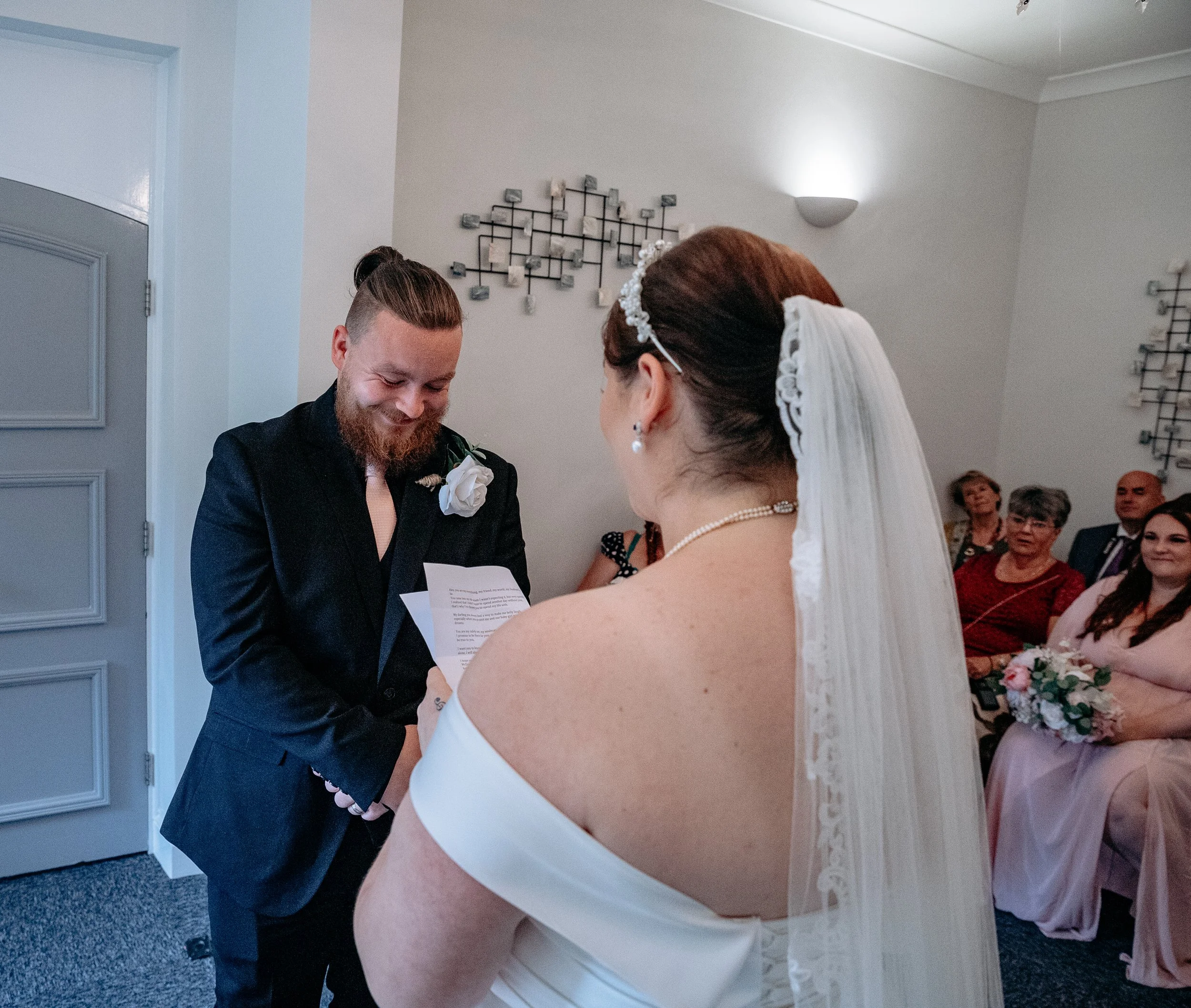 Bride and groom exchanging vows during wedding ceremony indoors, with guests seated in the background.