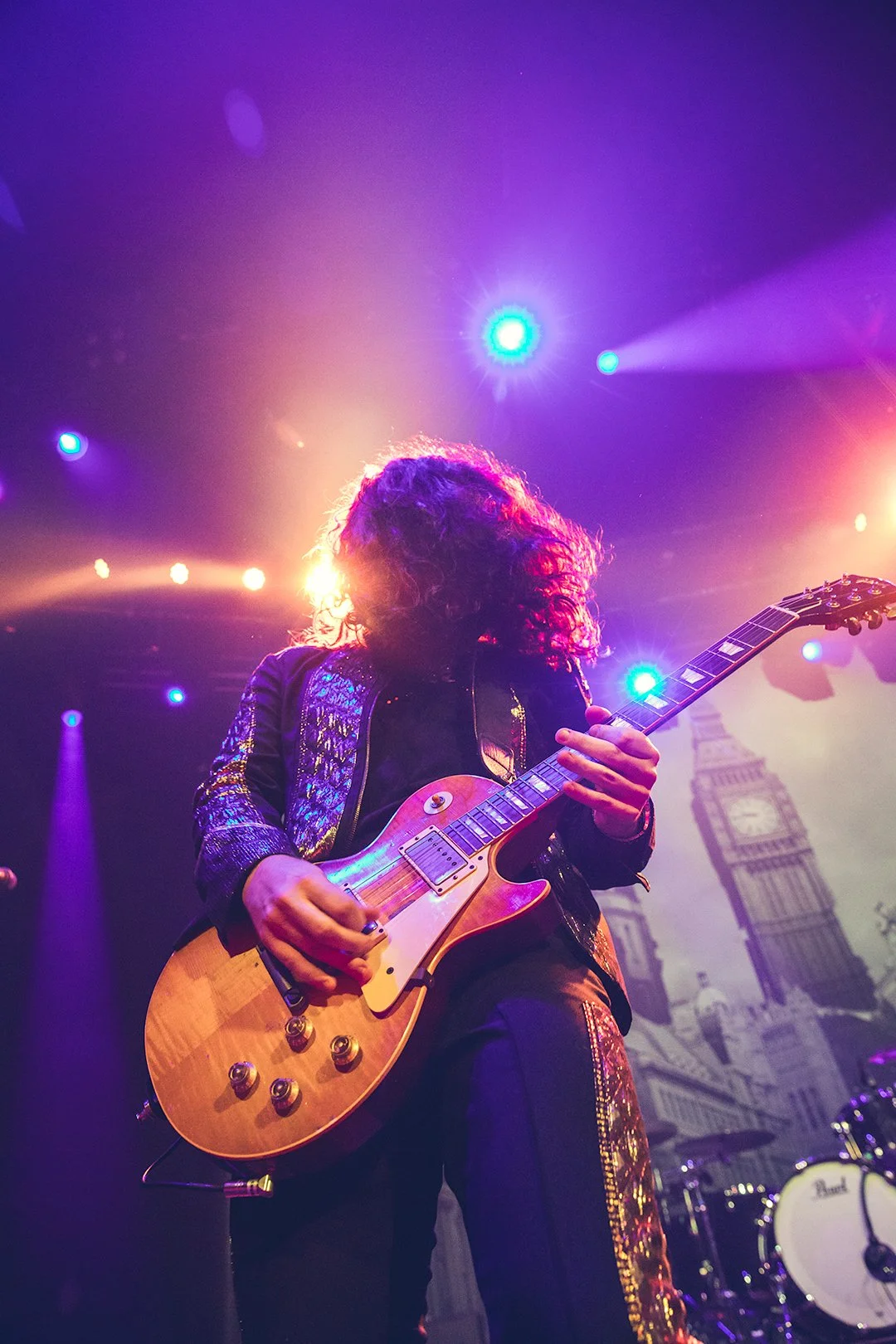 Guitarist playing an electric guitar on stage with colorful lights and a backdrop of Big Ben.