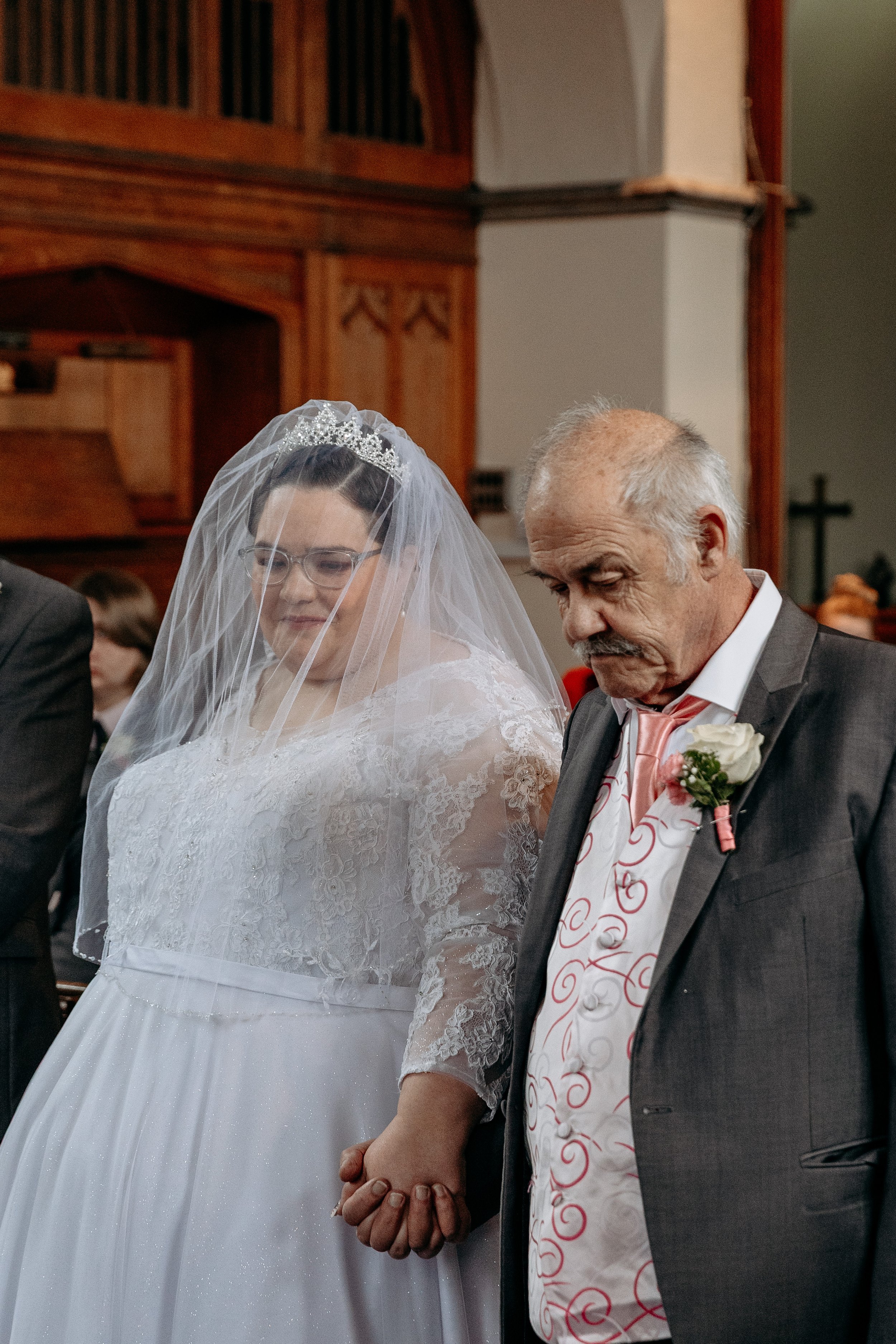 A bride and an older man holding hands during a wedding ceremony in a church.