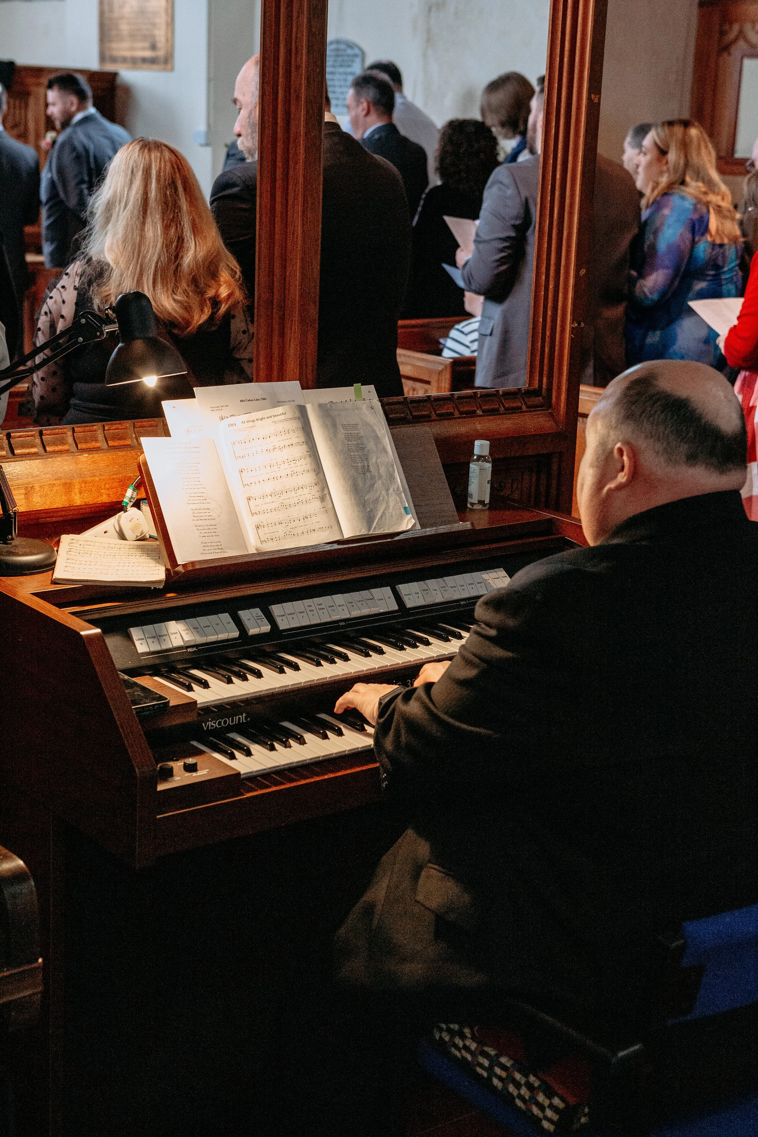 A man playing an electric organ during a church service with people standing and singing in the background.