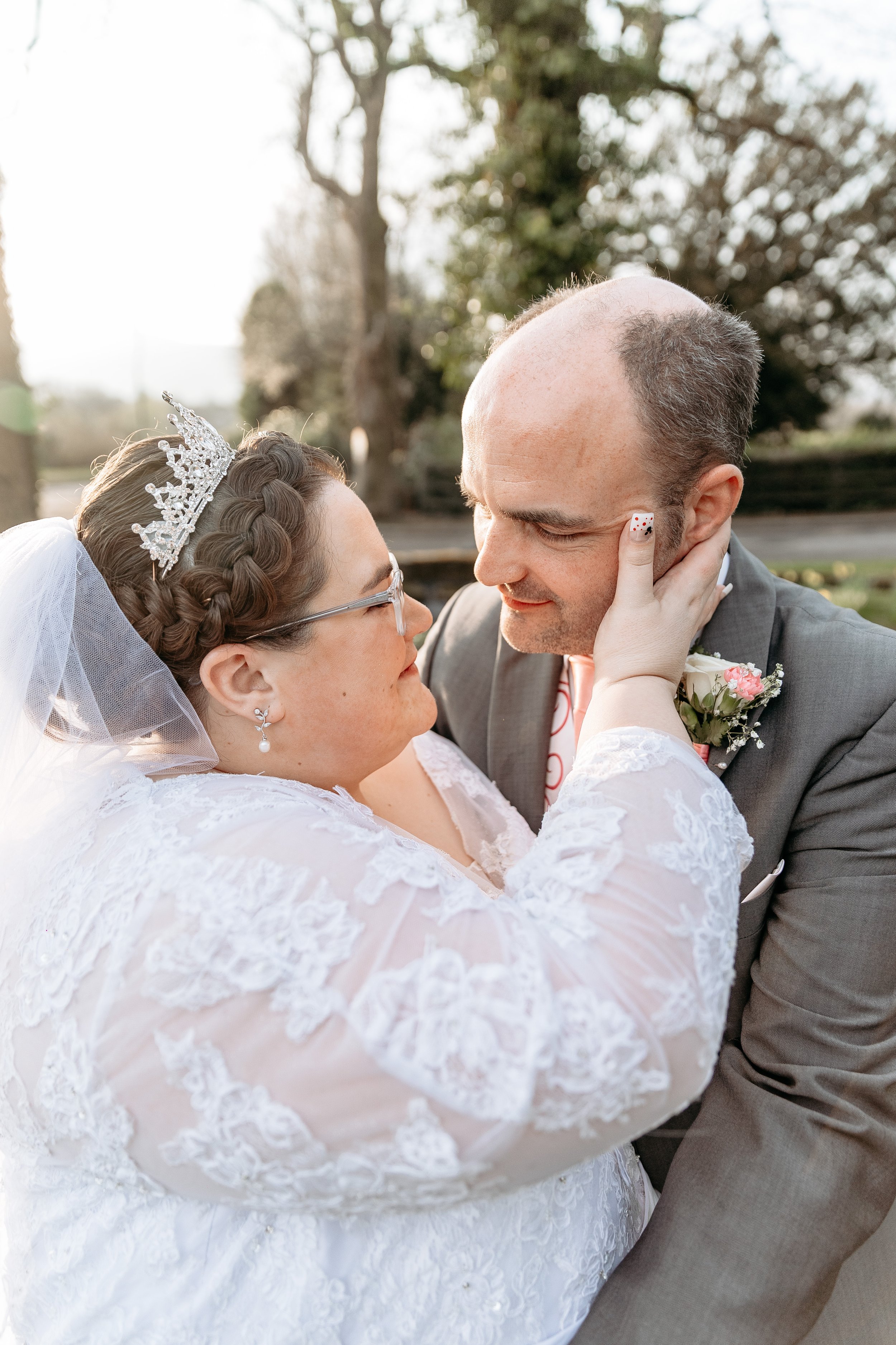 A bride and groom sharing an intimate moment outdoors during their wedding, with the bride gently holding the groom's face.