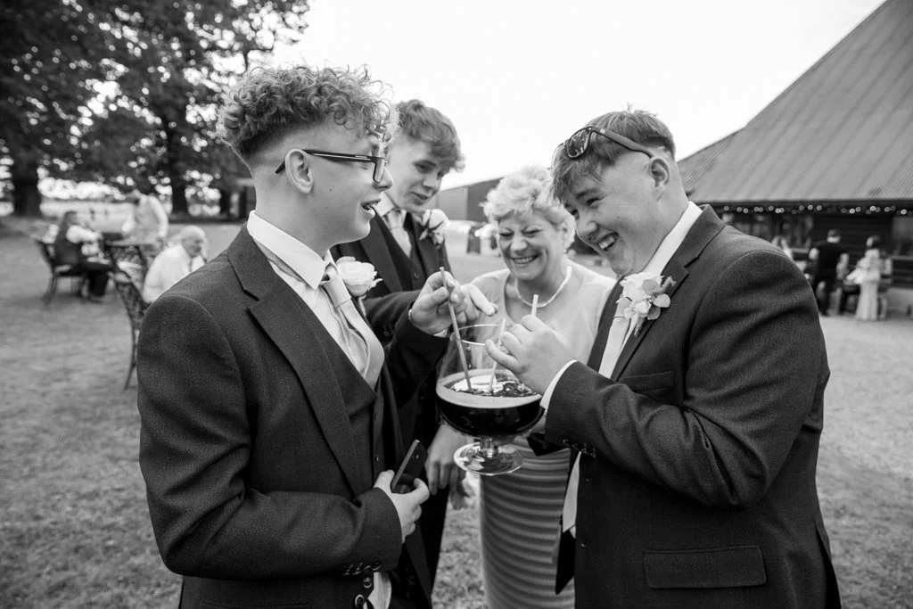 Group of four people in formal attire enjoying an outdoor celebration, with three men holding a drink and smiling.