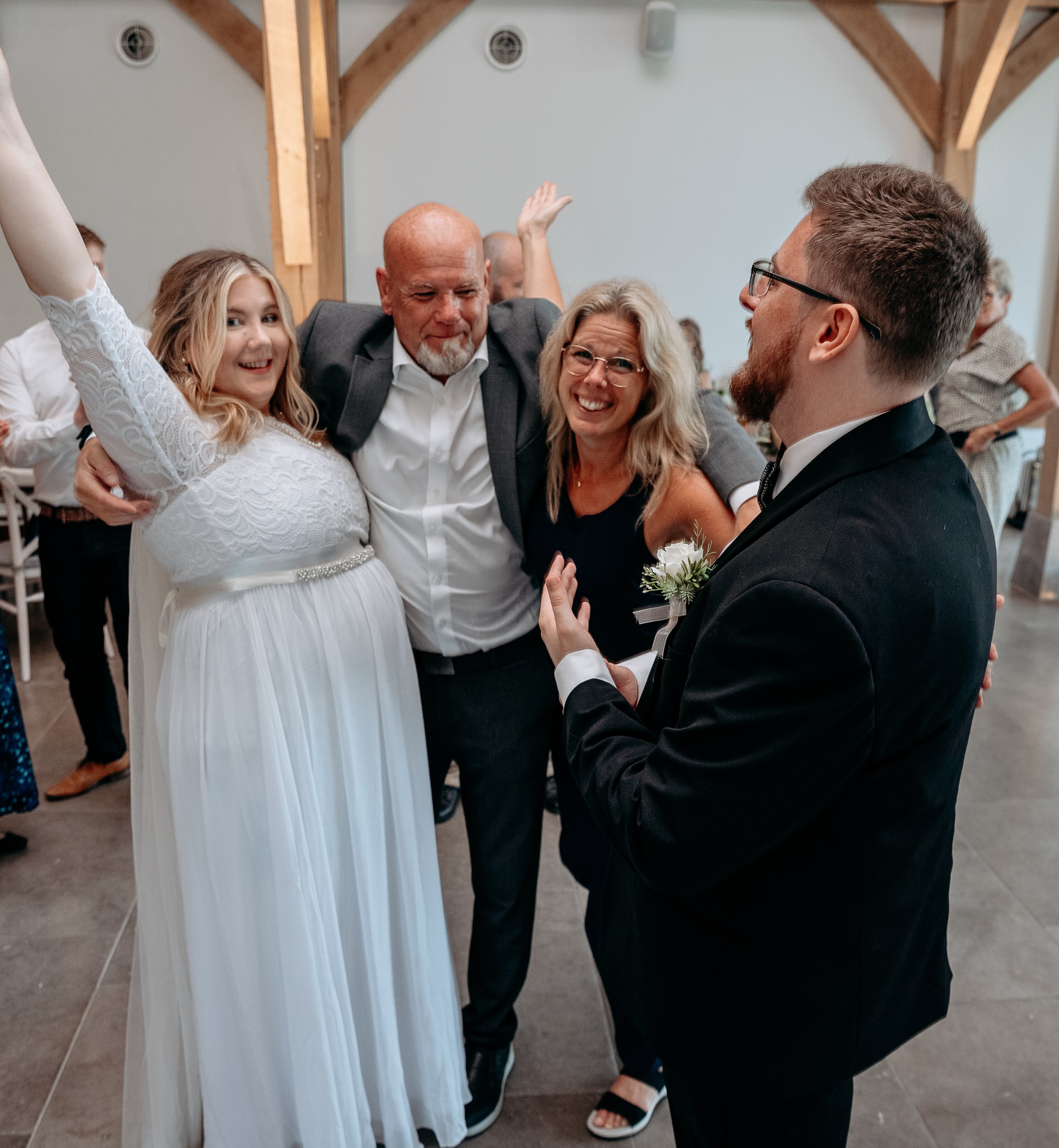 People celebrating at a wedding, featuring a bride in a white dress, a groom in a black suit, and two guests in joyful poses.