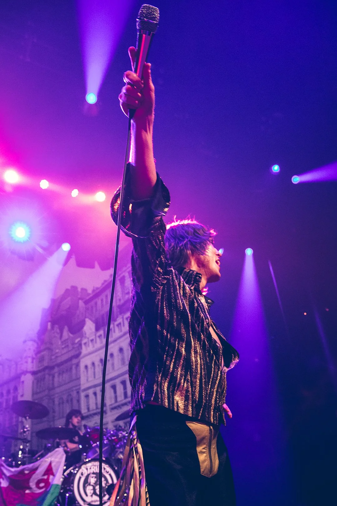 Performer holding microphone on stage with colorful lights.