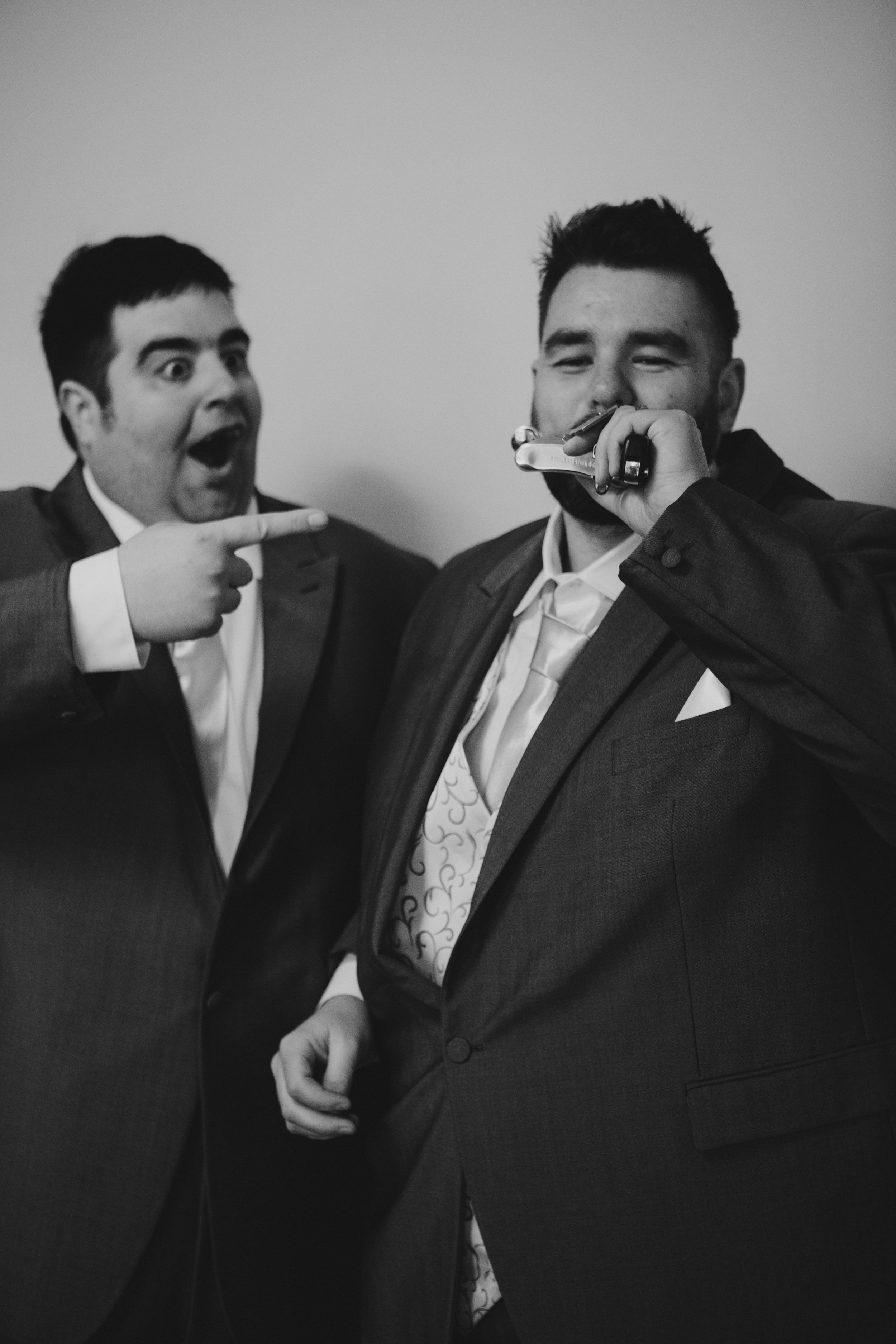 Two men in suits, one pointing at the other, who is holding a gun-shaped vape to his mouth, in a playful interaction.