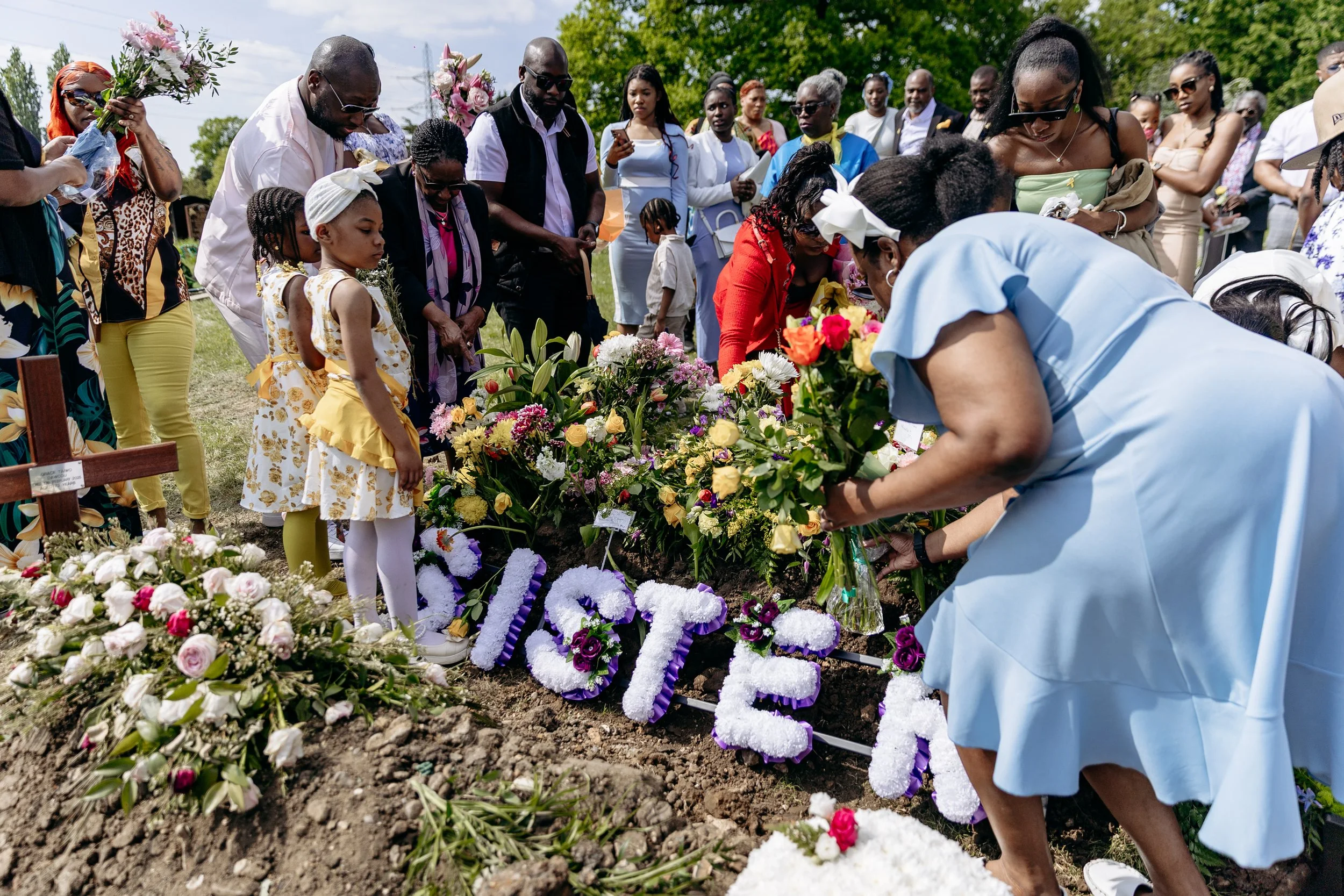 People at a funeral burying a loved one, with flowers and floral letters spelling 'LOVE' placed on the grave.