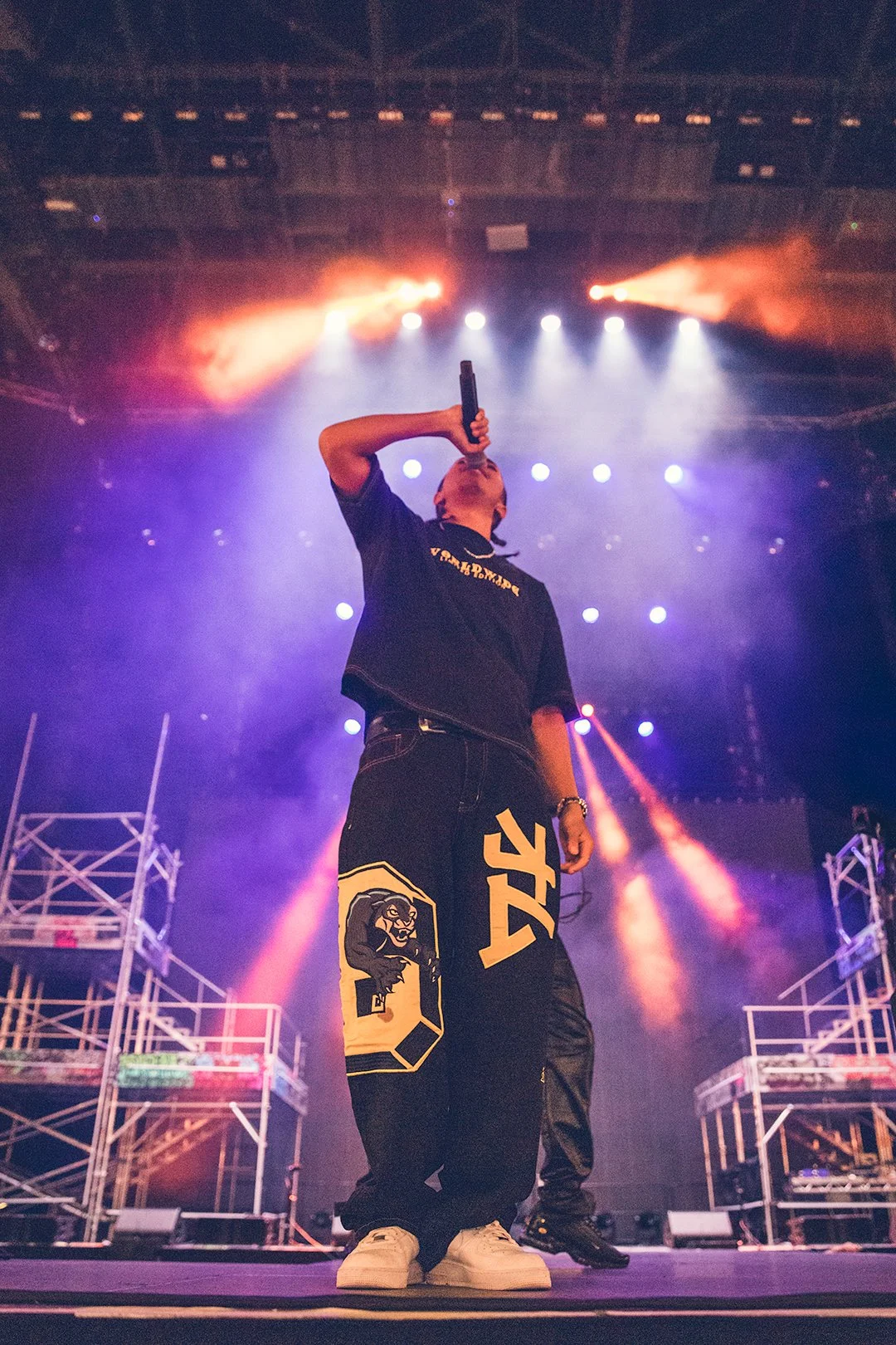 Performer singing on stage with colorful lights and scaffolding in the background