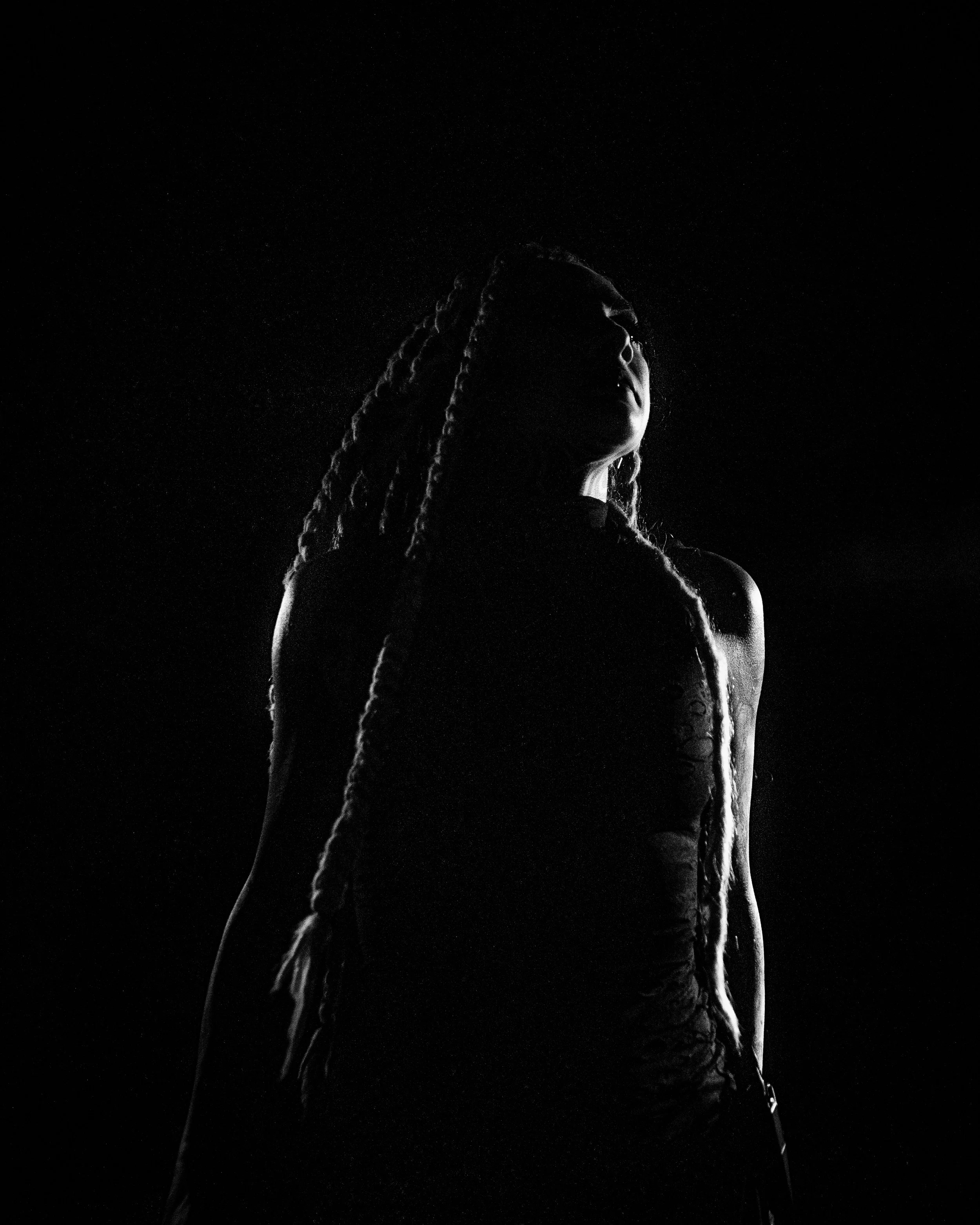 Silhouette of a woman with long braided hair against a black background, with dramatic lighting highlighting her outline.