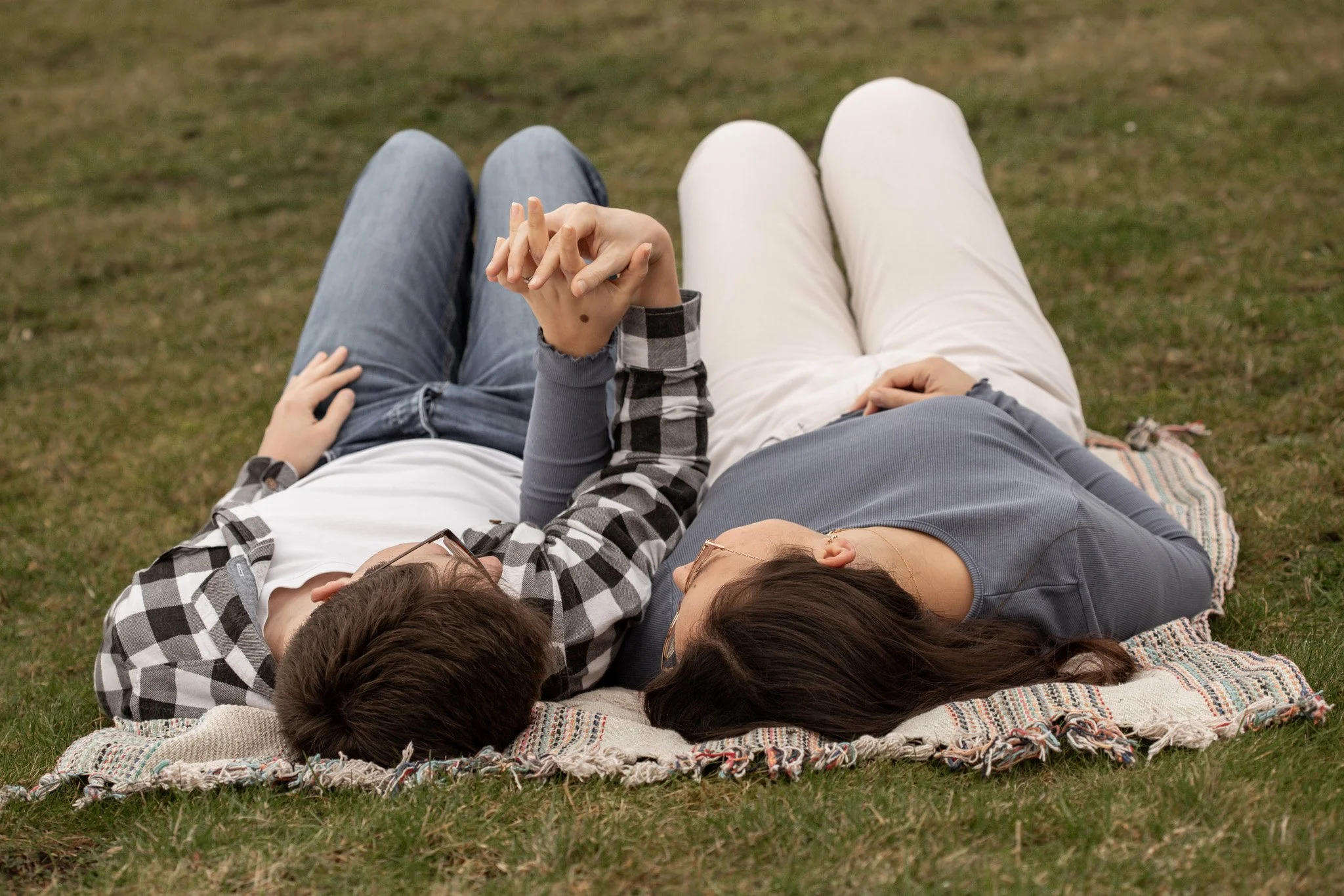 A couple lying on a blanket in a grassy area, holding hands and relaxing outdoors.