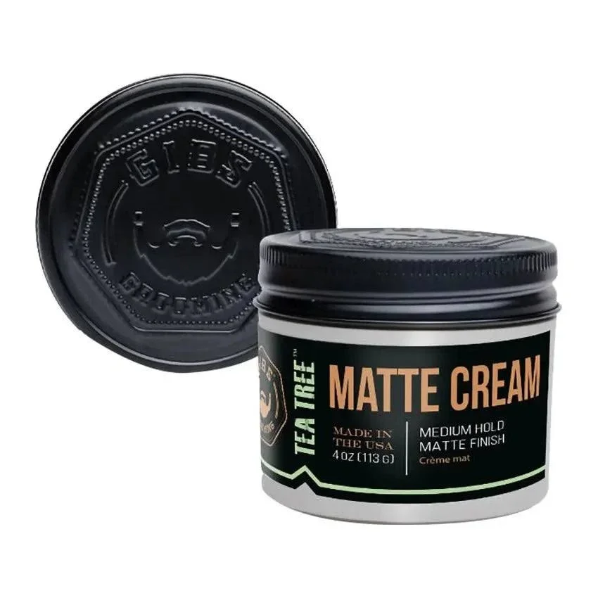 A small black jar of Tea Tree Matte Cream with a black lid, showing the label that reads 'Tea Tree Matte Cream, Made in the USA, 4 oz, Medium Hold, Matte Finish'. The lid is placed upside down behind the jar.