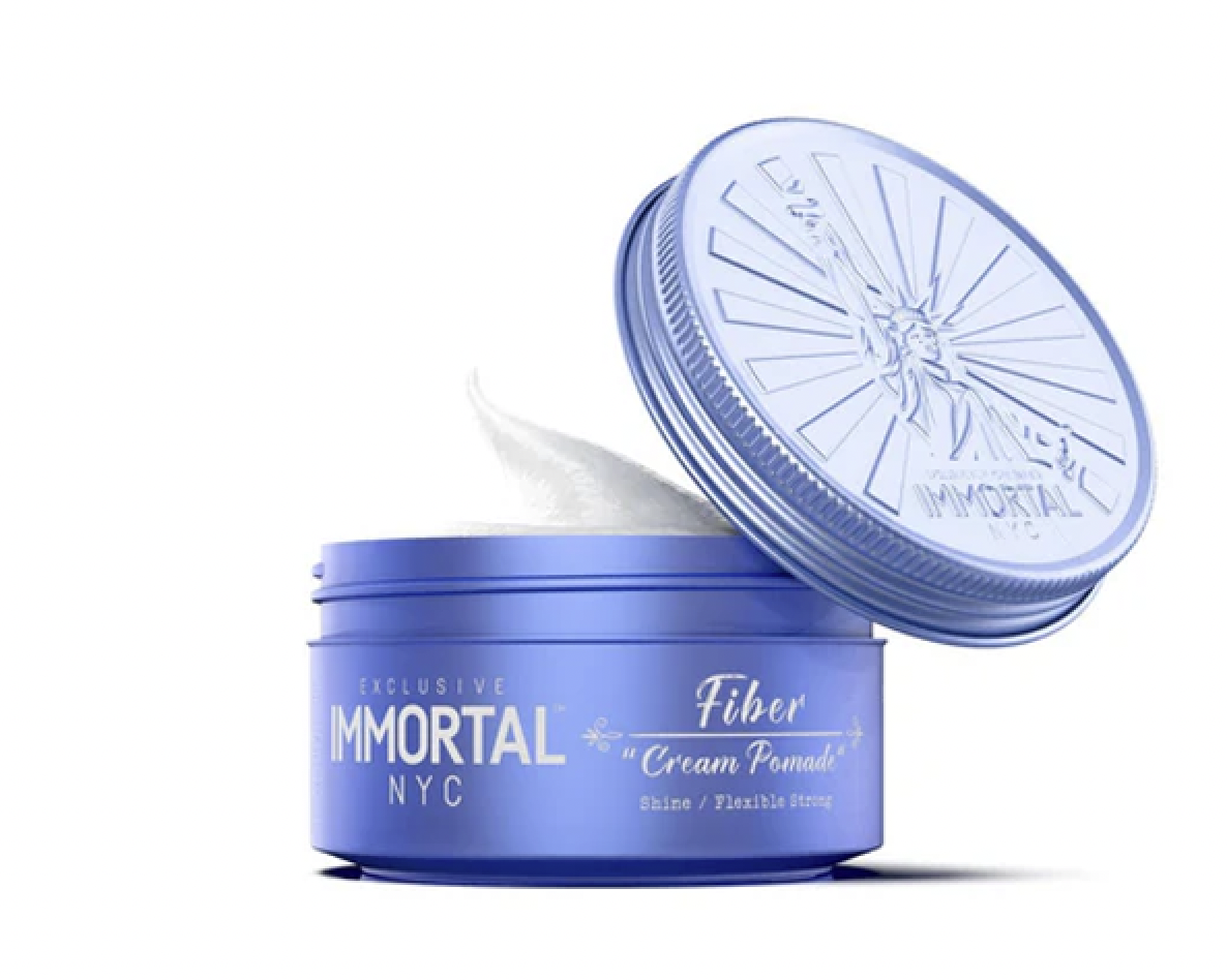 Blue container of Immortal NYC Fiber Cream Pomade with the lid partially open and white cream inside.