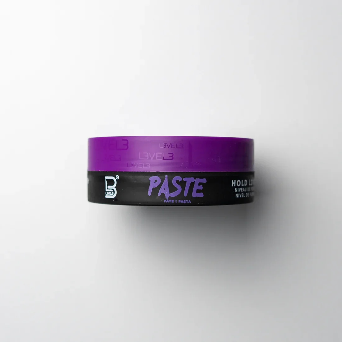 A round container labeled 'Paste' with a black bottom and purple lid, designed for hair styling or hair product use, on a white surface.