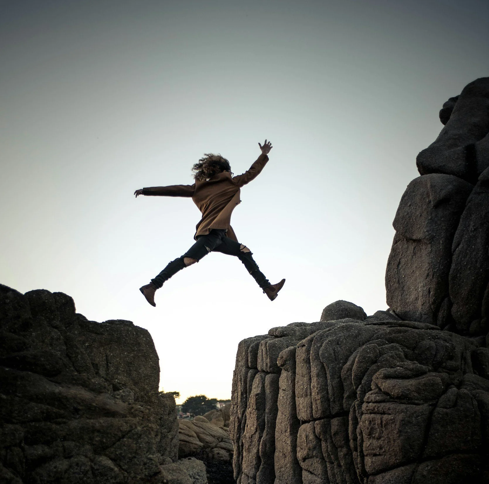Person jumping between rocks at sunset or dusk