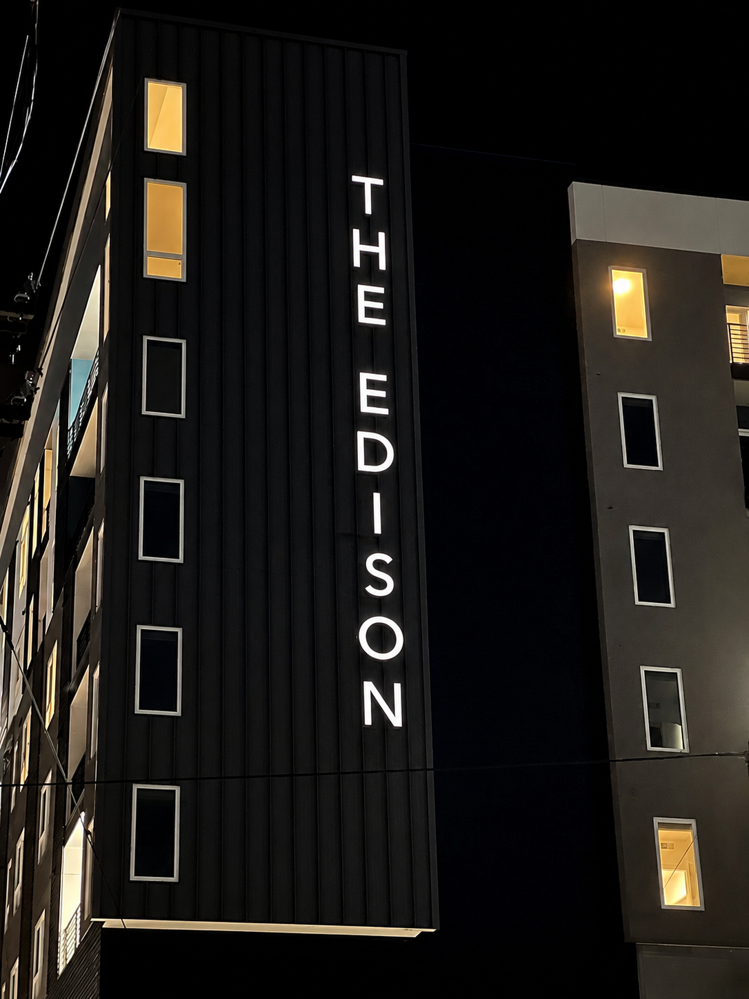 Night view of a modern multi-story hotel building with illuminated vertical sign reading 'THE EDISON' and lit windows.