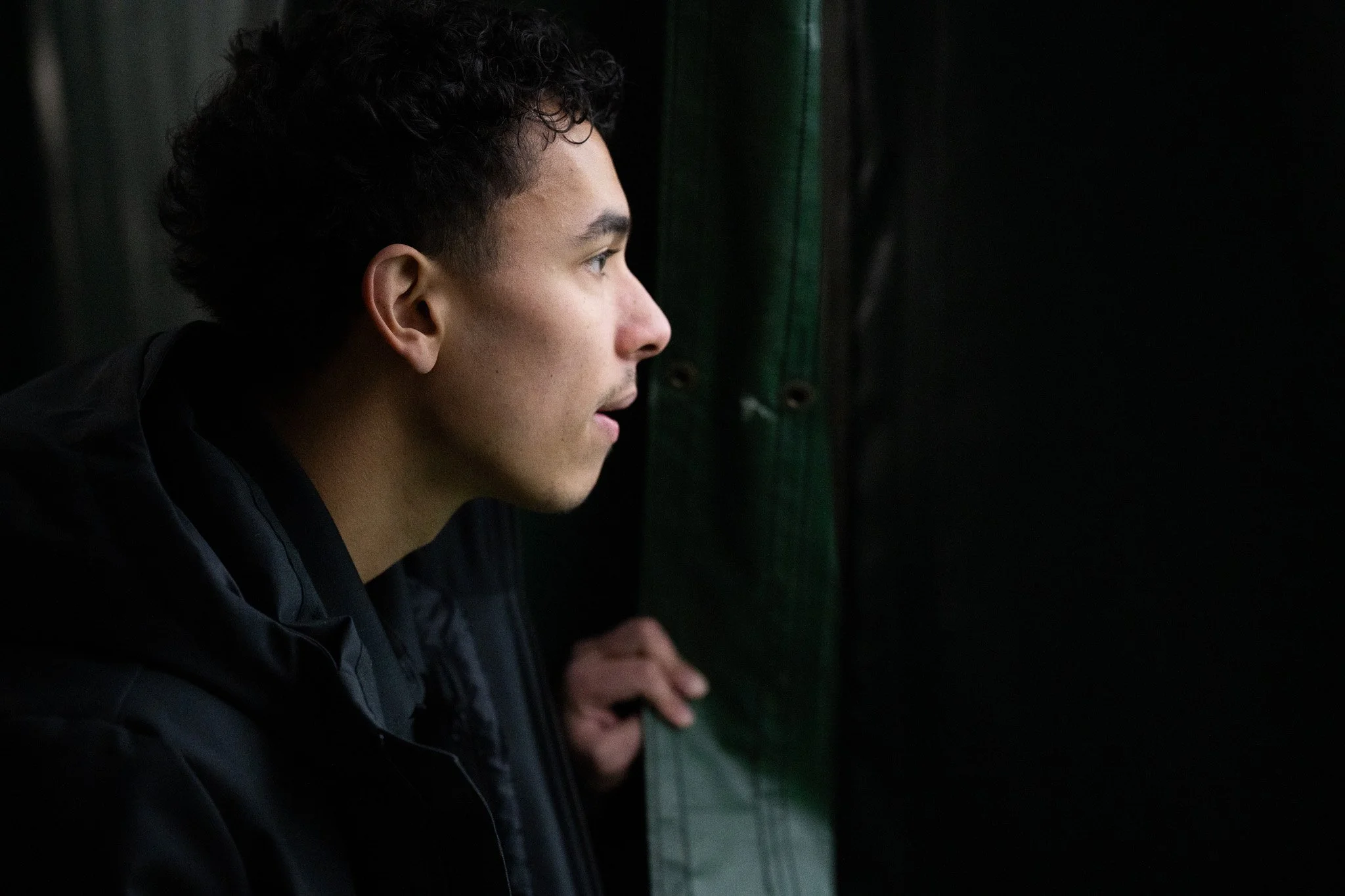 Sophomore Jensen Bicanic peers through the dividing tarp to watch his teammates' matches against Bellarmine University Jan. 24 at First Serve Muncie.