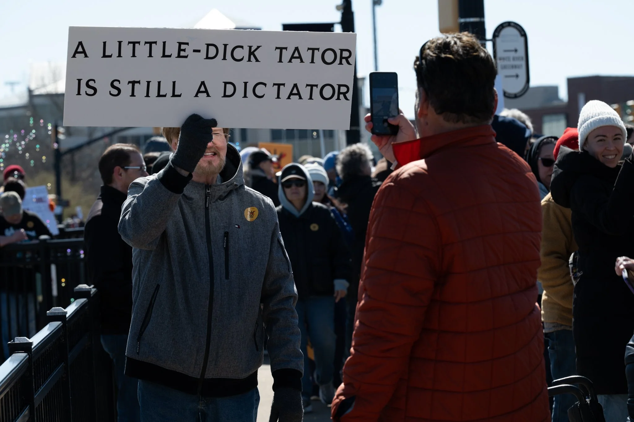 A protester hoists a sign while another snaps a photo during the ‘No Kings 3’ protest March 28 at the Fallen Heroes Memorial Bridge.